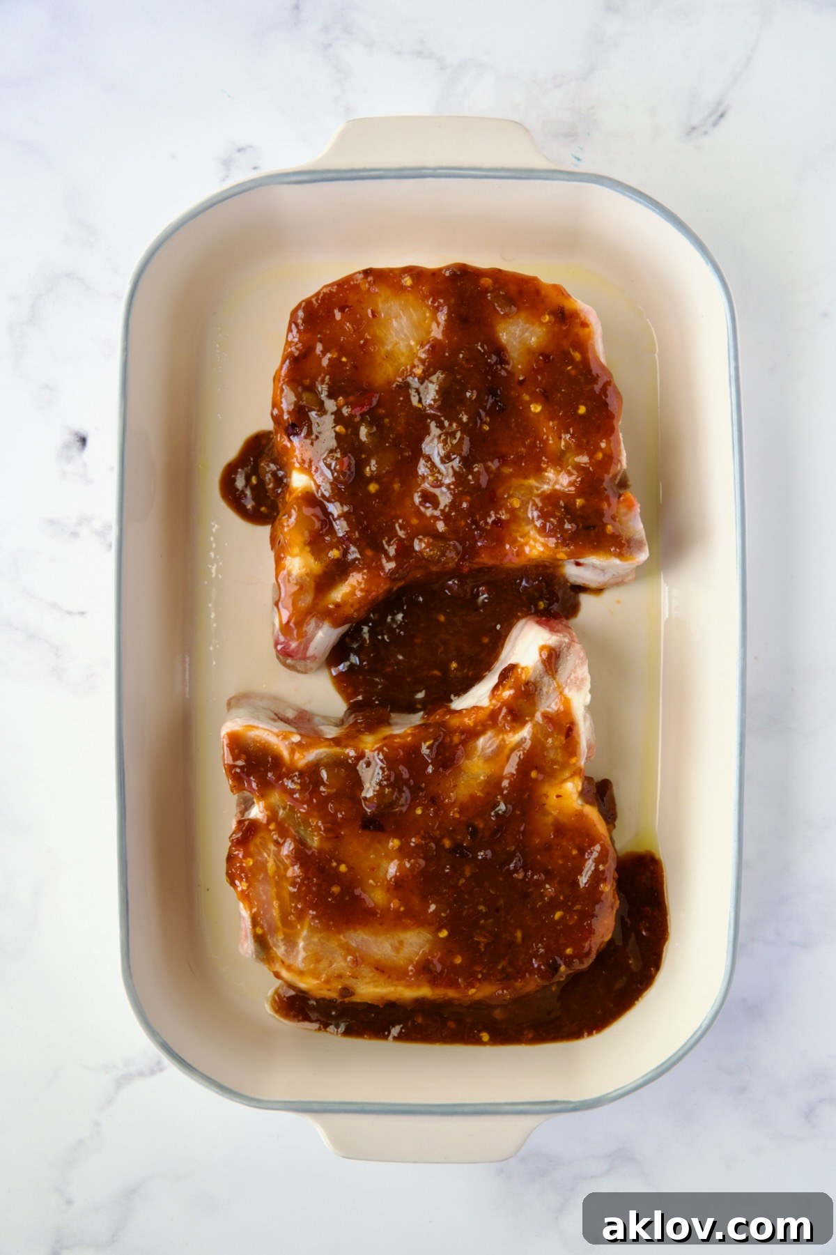 One pork chop in a baking dish, glistening with the first application of apricot-chili crisp glaze.