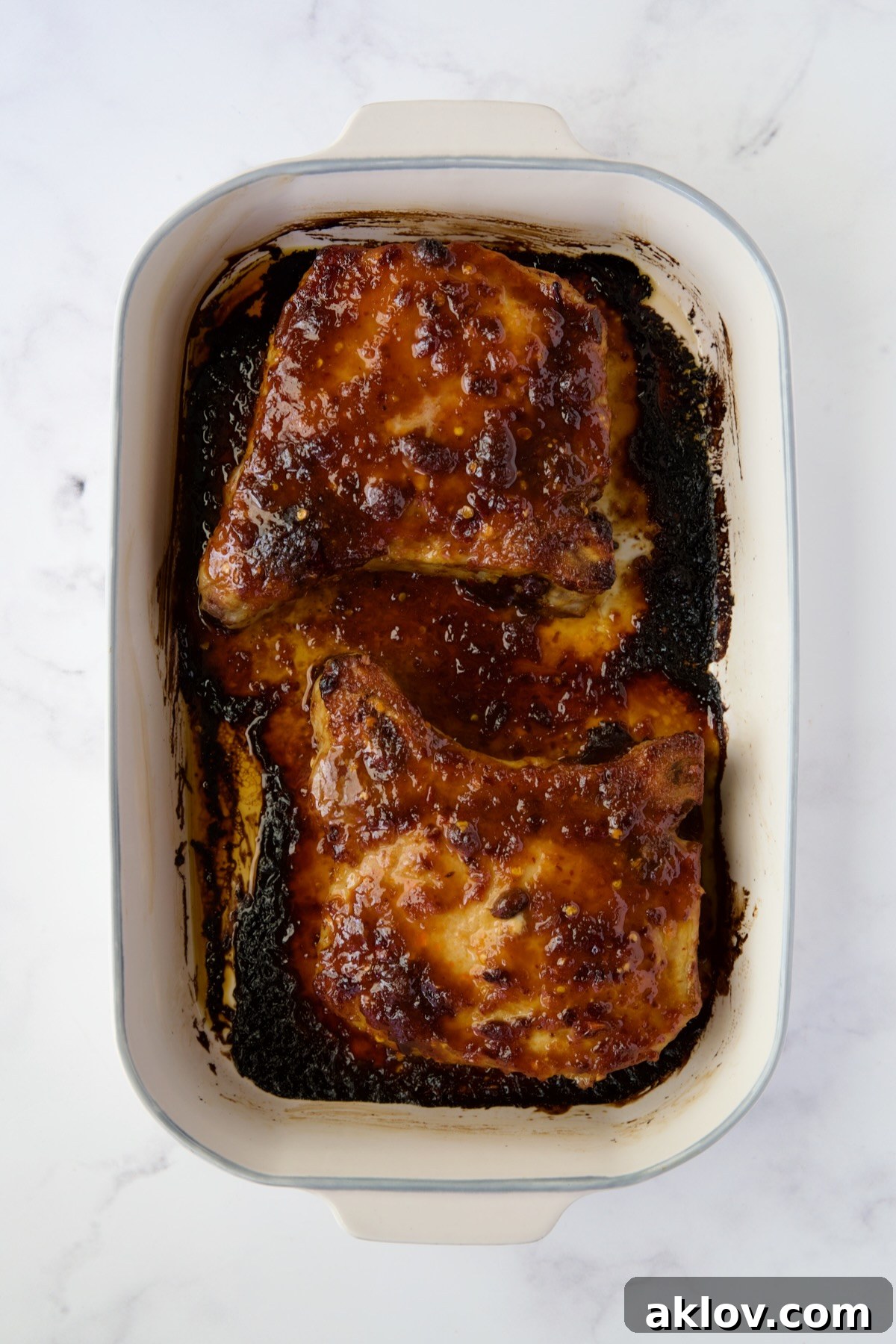 Two perfectly baked Asian Pork Chops, golden brown and glazed, resting in their baking dish after coming out of the oven.