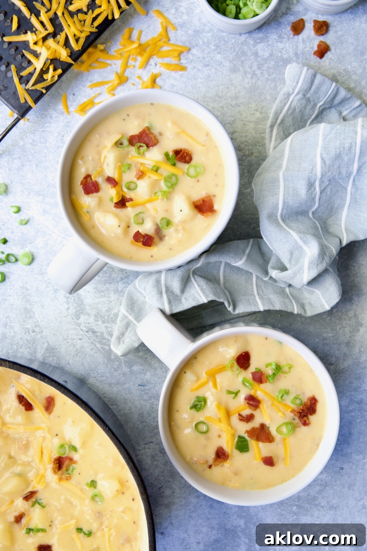 Two large soup mugs of Cheddar Bacon Potato Soup garnished with bacon and scallion.