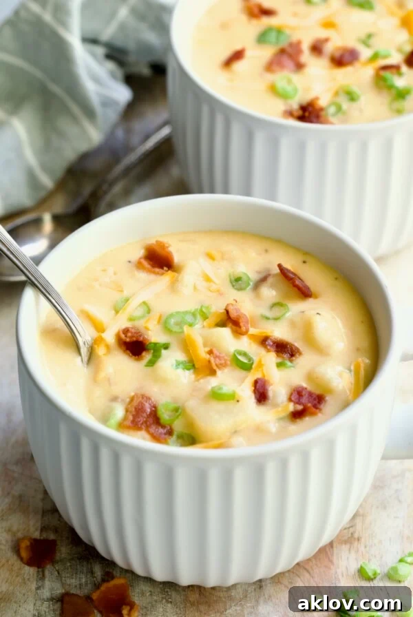 Cheddar Bacon Potato Soup in large white soup mug with spoon garnished with bacon, scallions and cheese shreds.