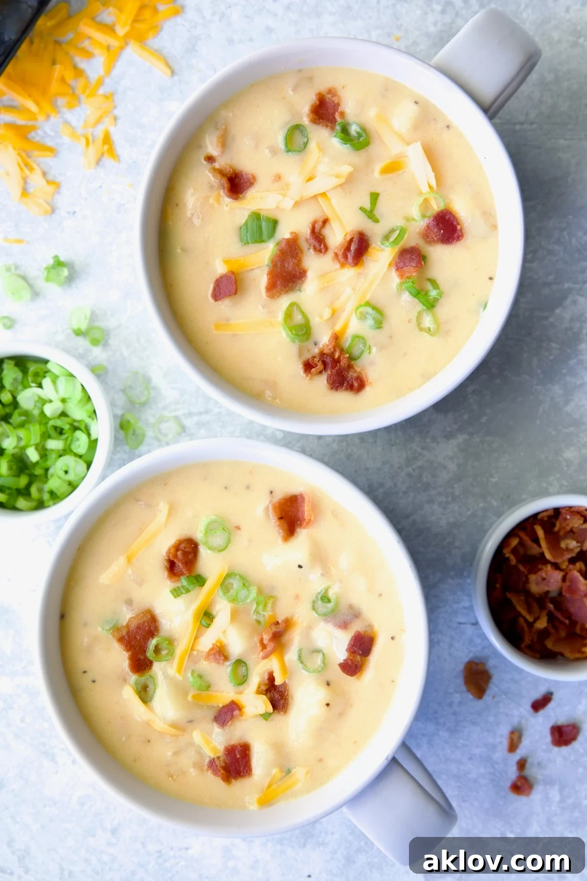 Two large soup mugs of Cheddar Bacon Potato Soup garnished with bacon and scallion.