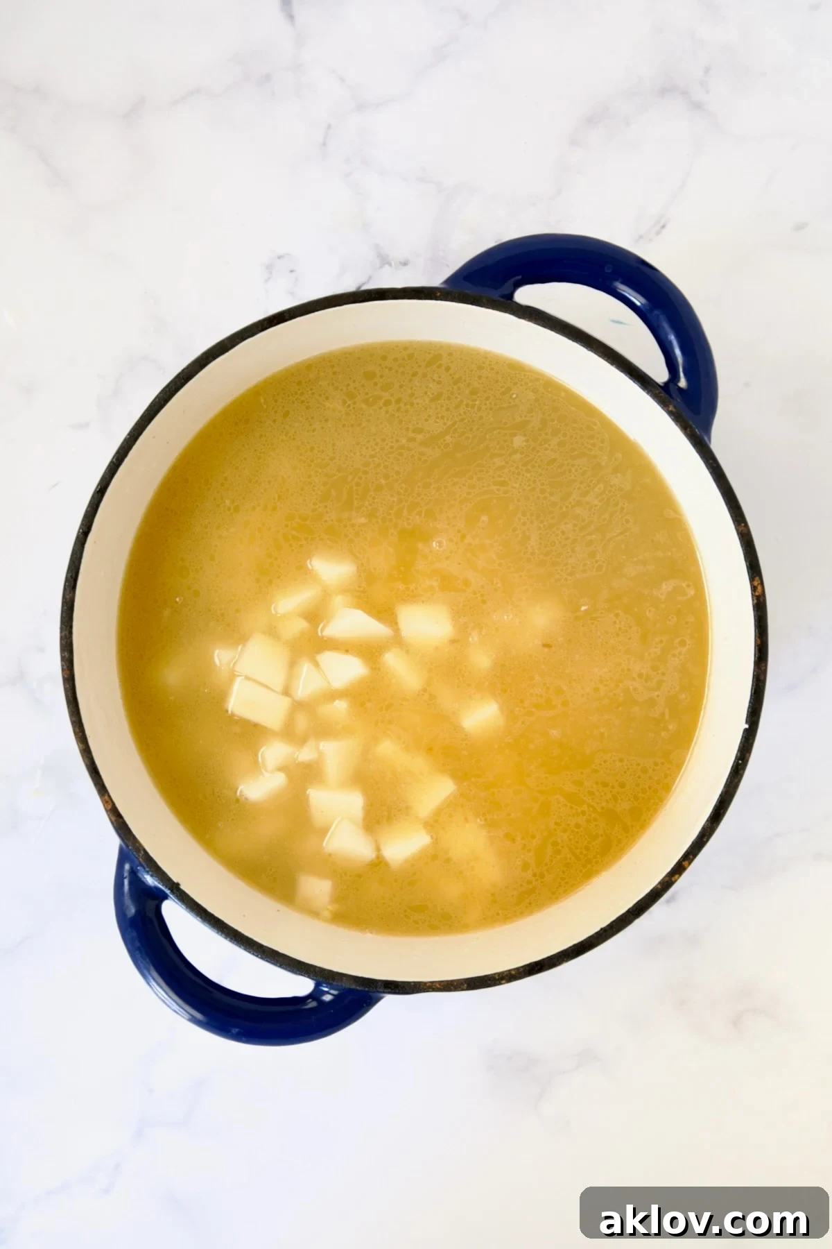 Potatoes added to broth in blue Dutch oven.