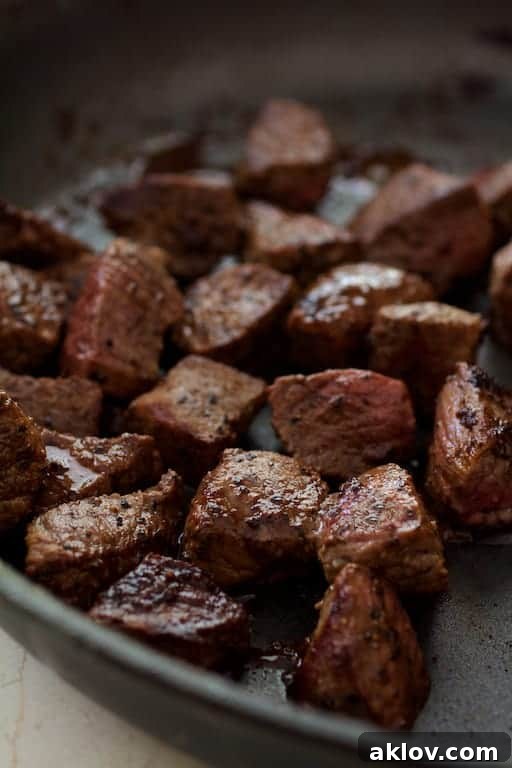 Close-up photo of perfectly browned beef cubes searing in a saute pan, exhibiting a rich, caramelized crust.