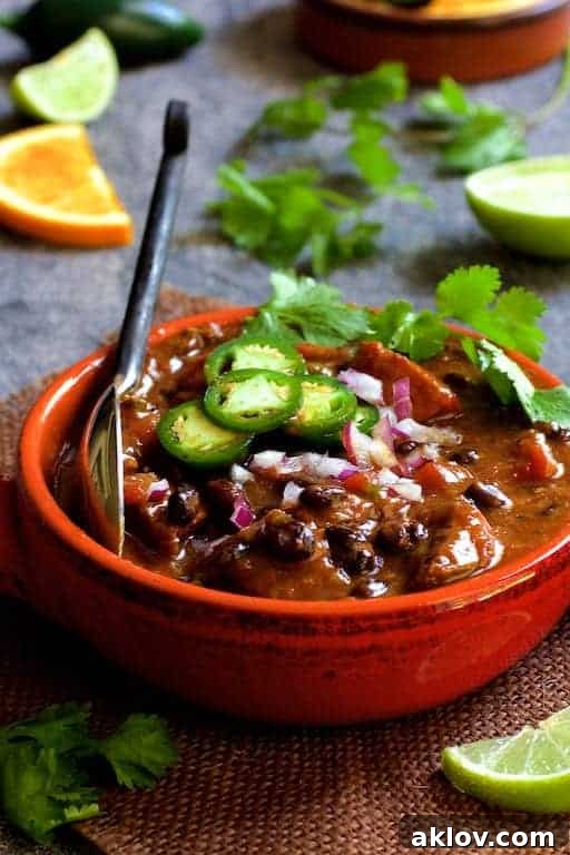 Feijoada (Brazilian Beef Stew) in a red bowl garnished with jalapeno slices, cilantro and lime wedges.