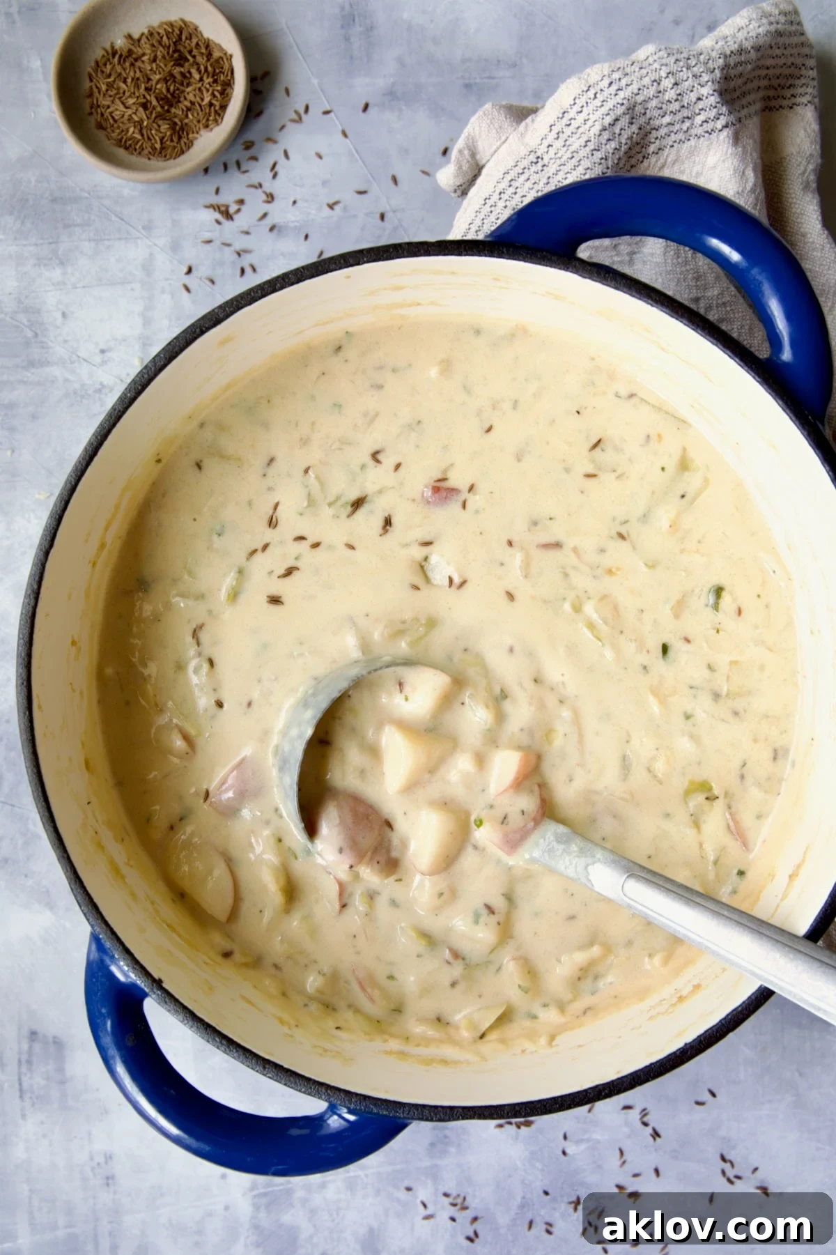 The completed Cabbage and Potato Soup, garnished with fresh herbs and more caraway seeds, served elegantly in a blue cast iron Dutch oven.