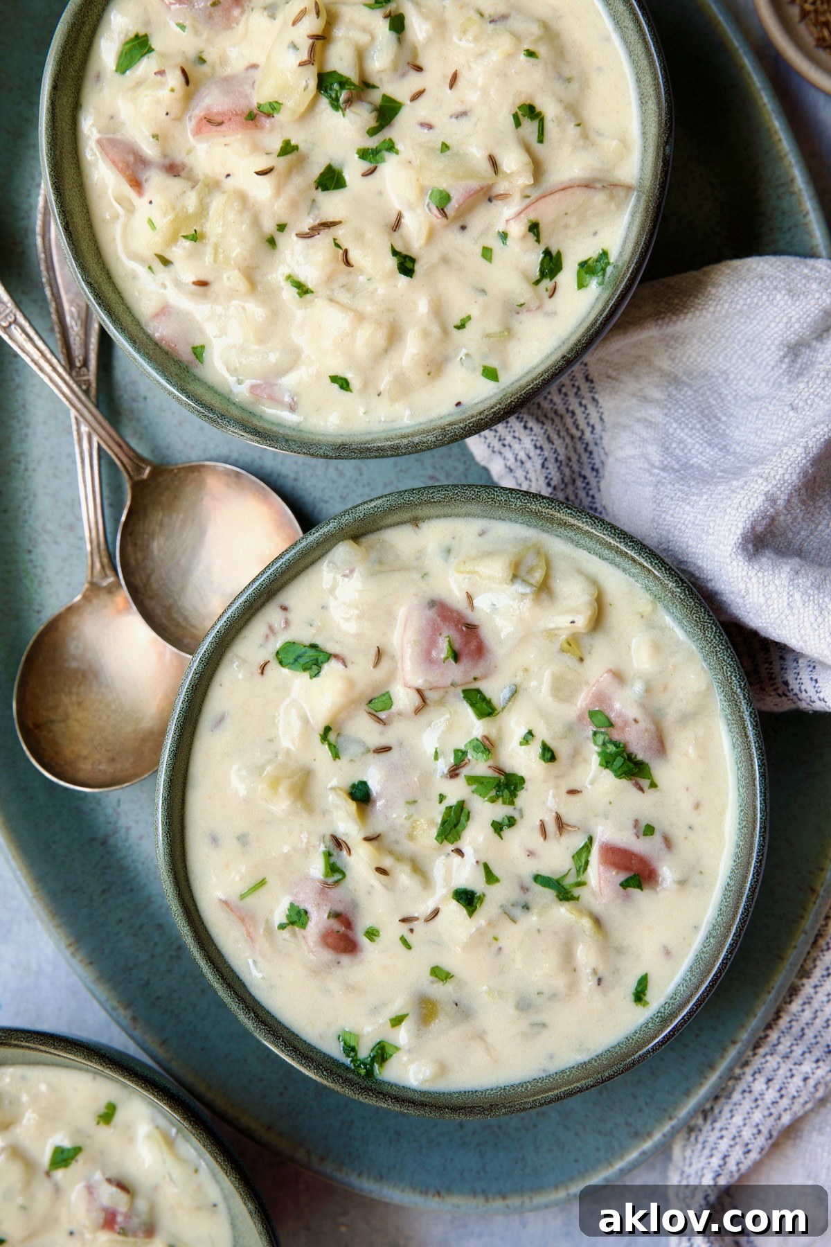 Two enticing bowls of Creamy Cabbage and Potato Soup arranged on a green oval platter, accompanied by two elegant soup spoons, inviting indulgence.