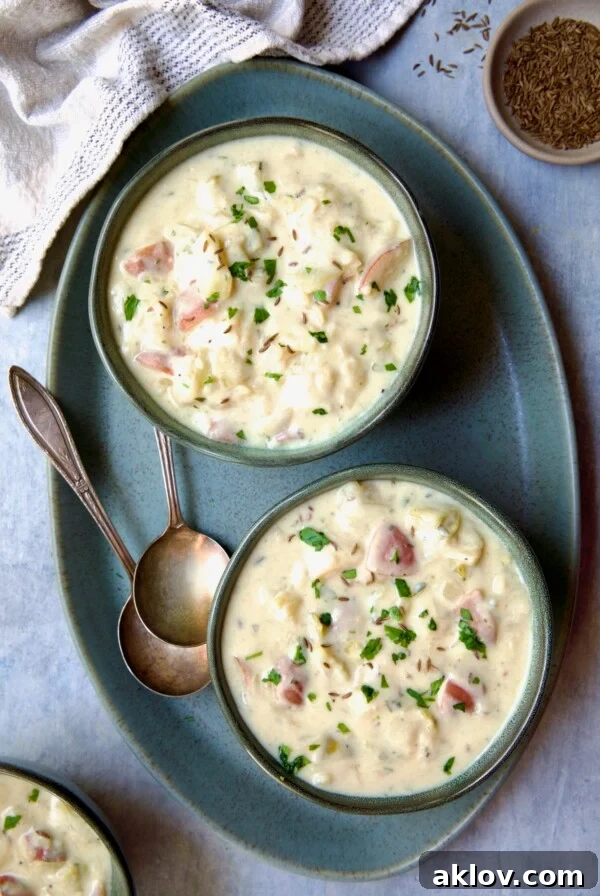 Two bowls of Creamy Cabbage and Potato Soup on a green oval platter with two soup spoons.