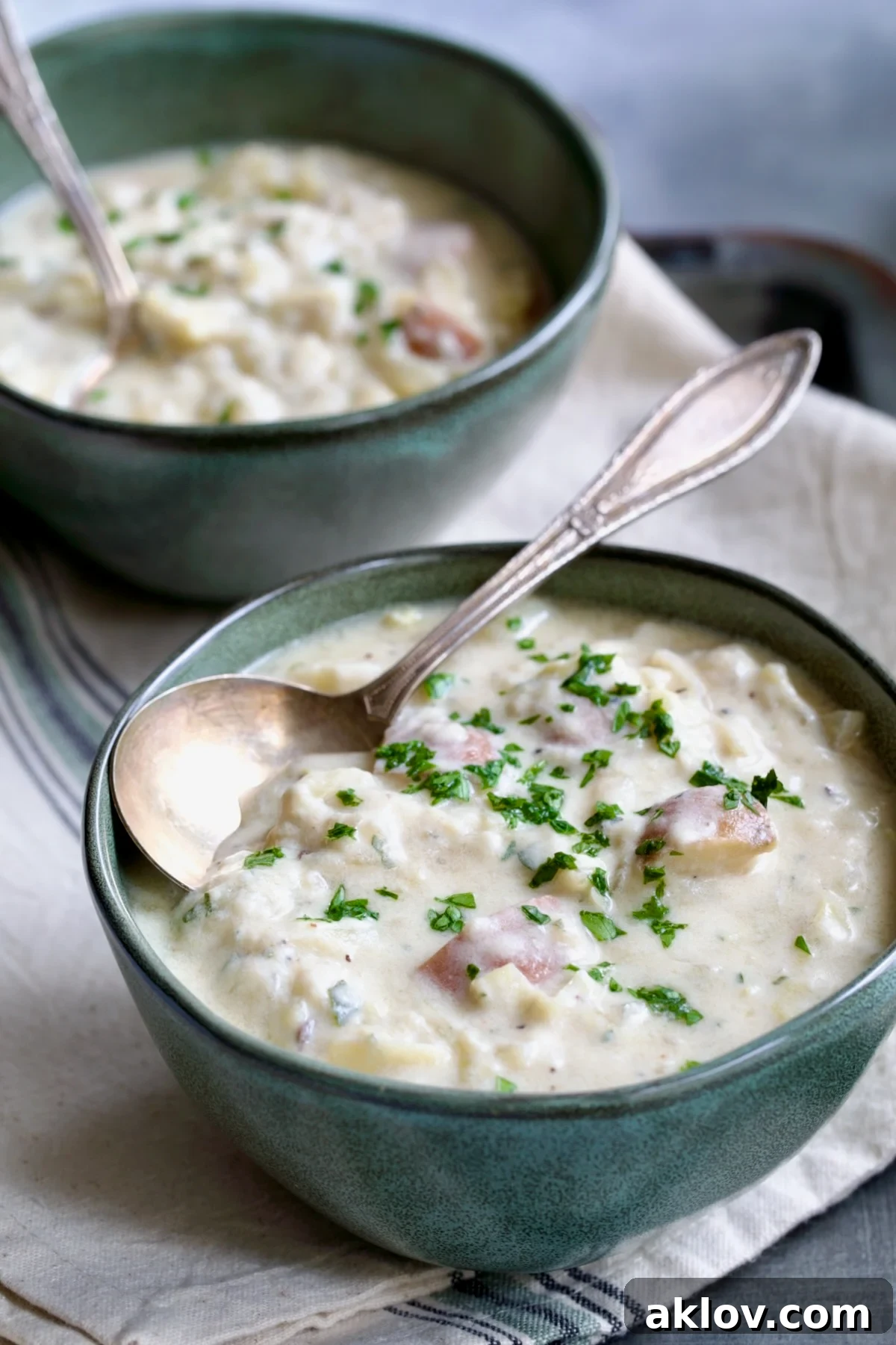 Two bowls of Creamy Cabbage and Potato Soup resting on a striped towel, with two soup spoons beside them.