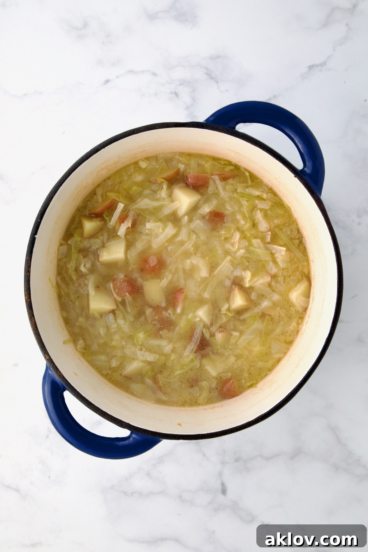 Chicken broth generously poured over the simmering onions, cabbage, and potatoes in a blue cast iron Dutch oven.