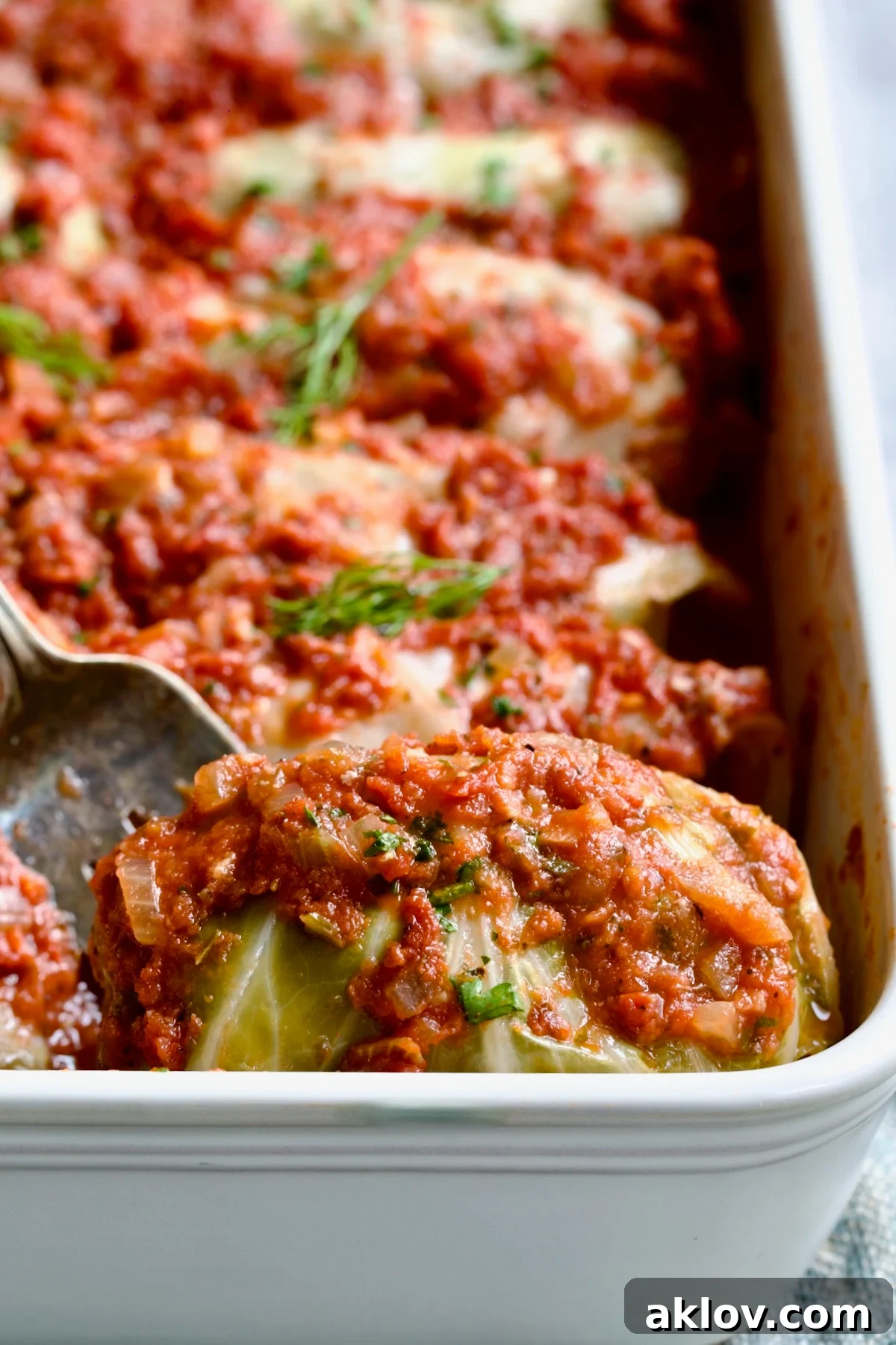 Serving fork picking up a Polish Stuffed Cabbage roll from white baking dish.