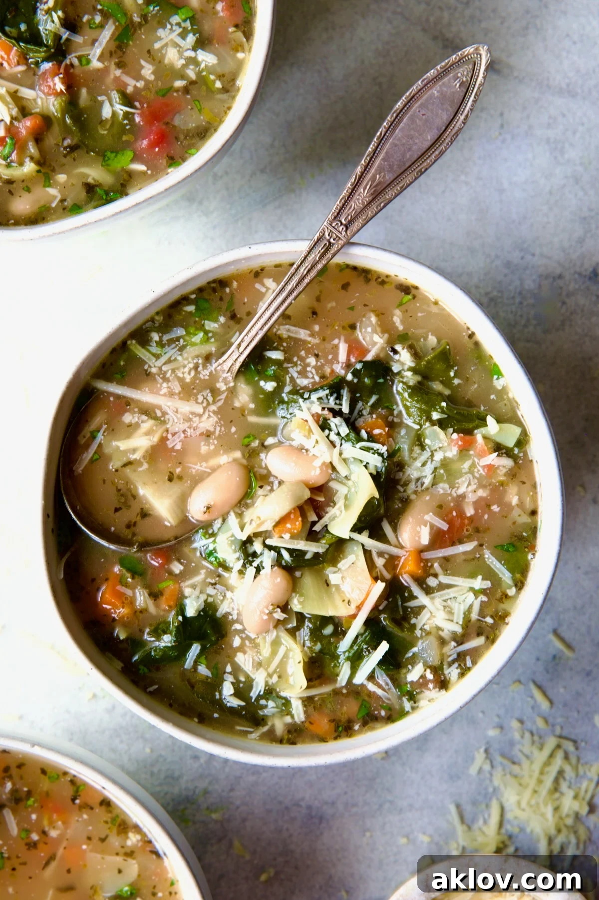 Vegetable Bean Soup in white bowl with spoon, garnished with fresh herbs and Parmesan.