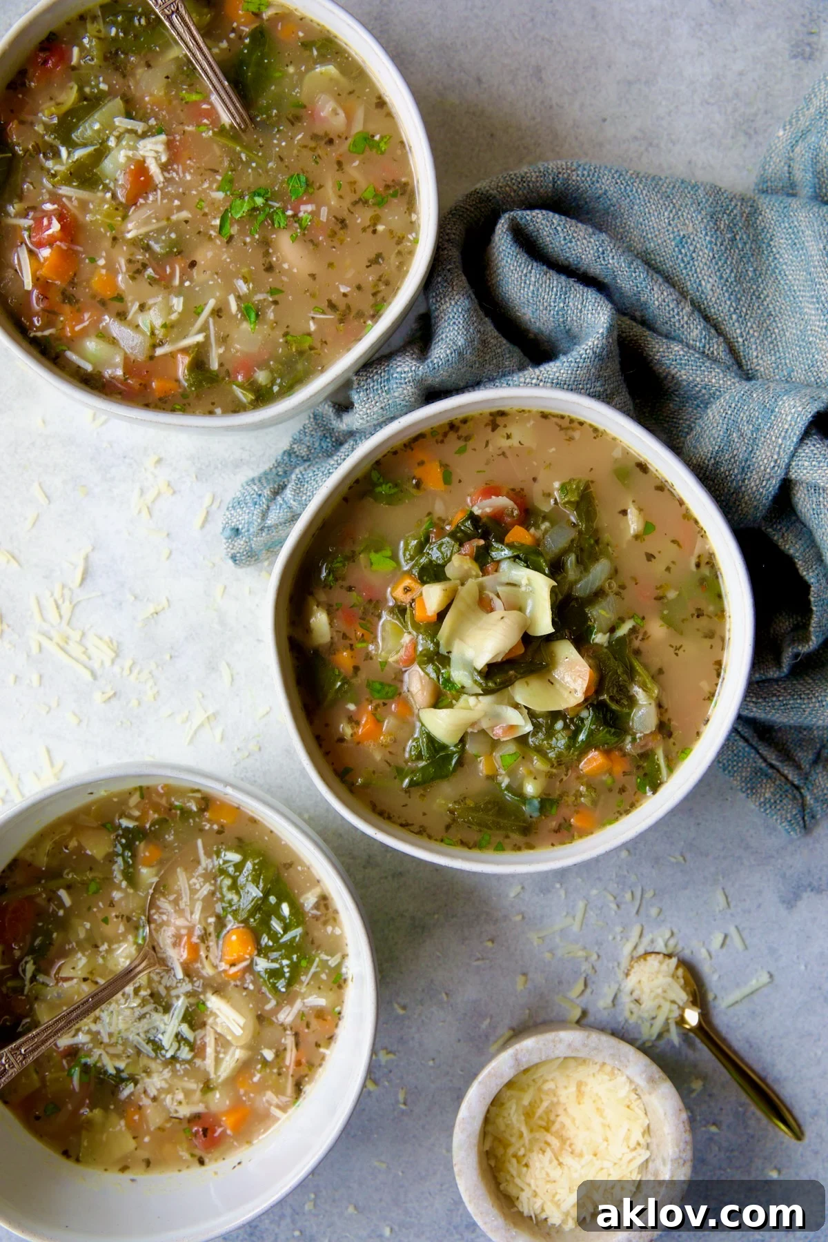 Three bowls of Vegetable Bean Soup, garnished with Parmesan cheese and fresh herbs, arranged beautifully with a light blue napkin.