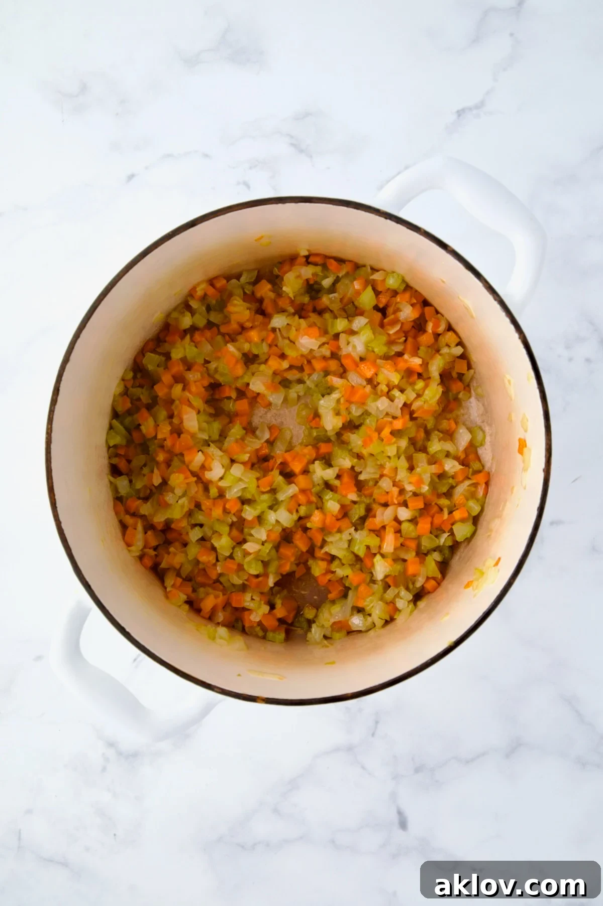 Softened onions, celery, and carrots gently cooking in a white Dutch oven.