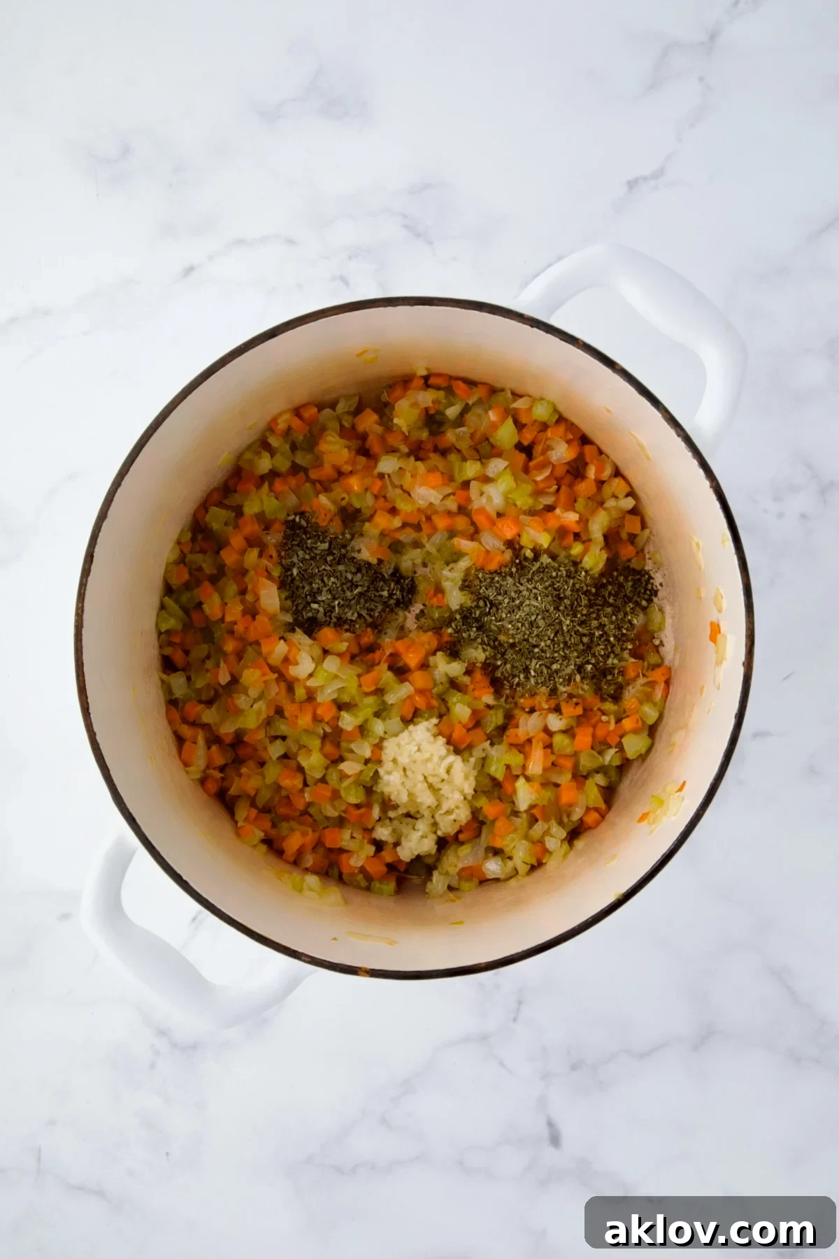 Aromatic garlic and herbs added to the softened vegetables in a white Dutch oven.