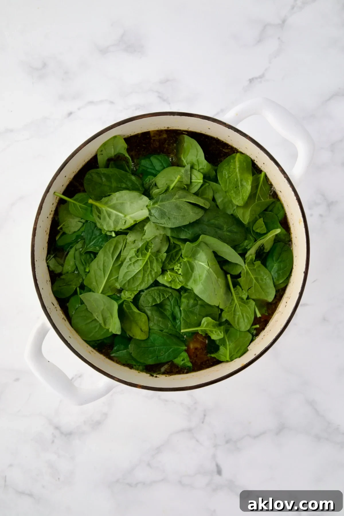 Fresh spinach being added to the hot Vegetable Bean Soup in a white Dutch oven.
