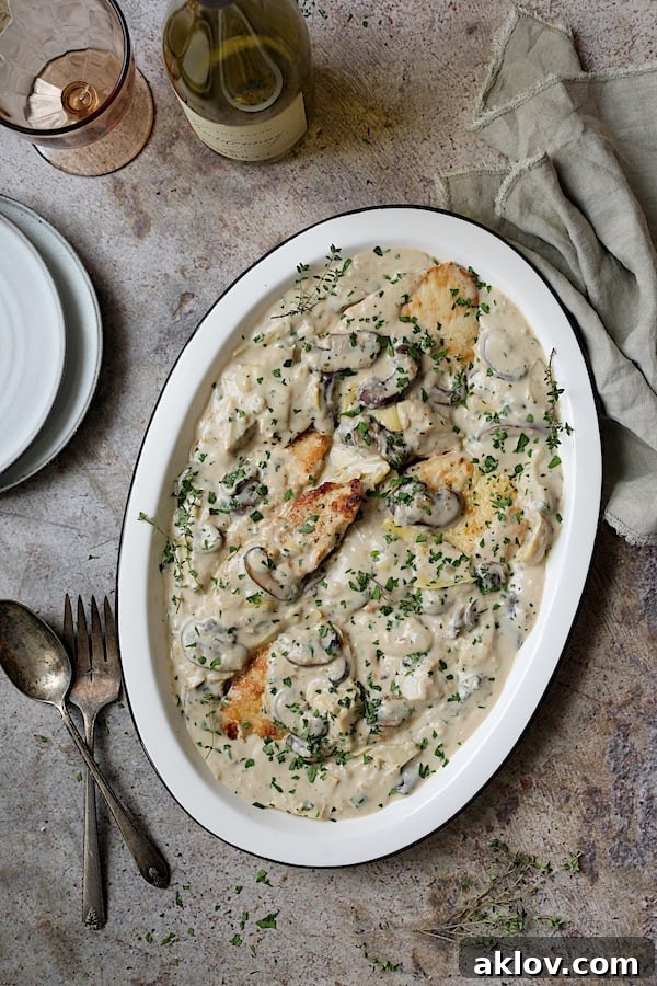 Turkey Scallopini in Sherry Cream Sauce with Mushrooms and Artichokes - Overhead shot of finished dish with platter at an angle with wine bottle, glass, serving utensils and napkin