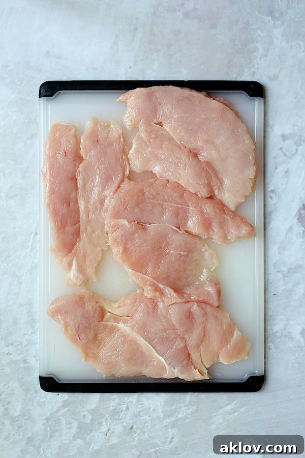 Overhead shot of turkey cutlets on white plastic cutting board, ready for pounding