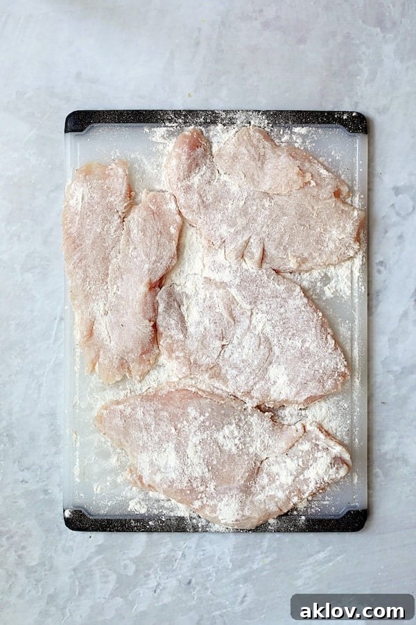Overhead shot of turkey cutlets on white cutting board that have been dredged in flour