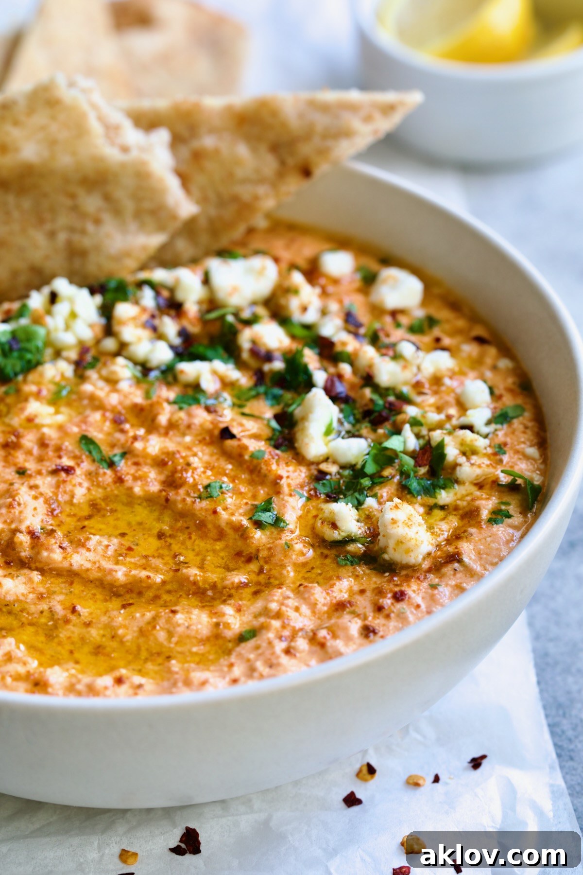 Spicy Feta Dip (Tirokafteri) in white bowl garnished with crumbled feta cheese and parsley surrounded by pita wedges.