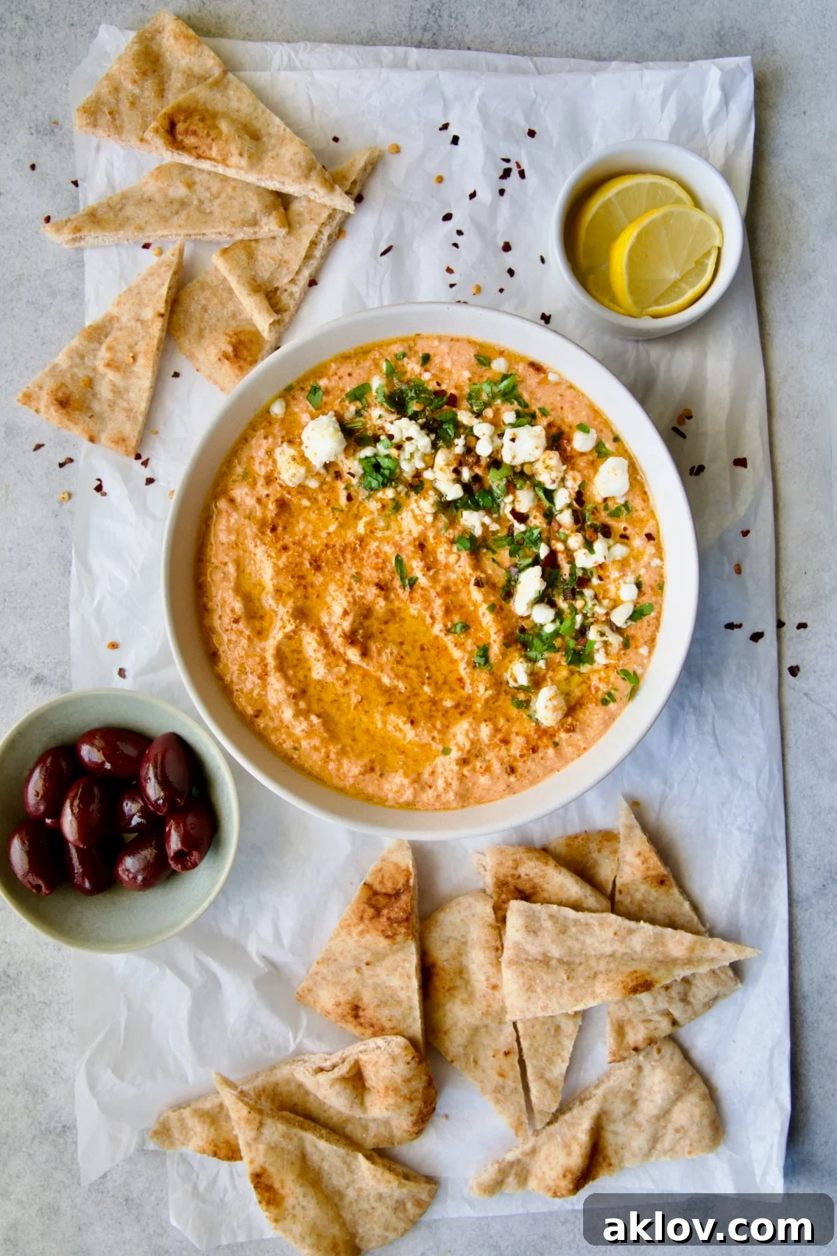 Spicy Feta Dip (Tirokafteri) in white bowl on parchment paper garnished with crumbled feta cheese and parsley surrounded by pita wedges.