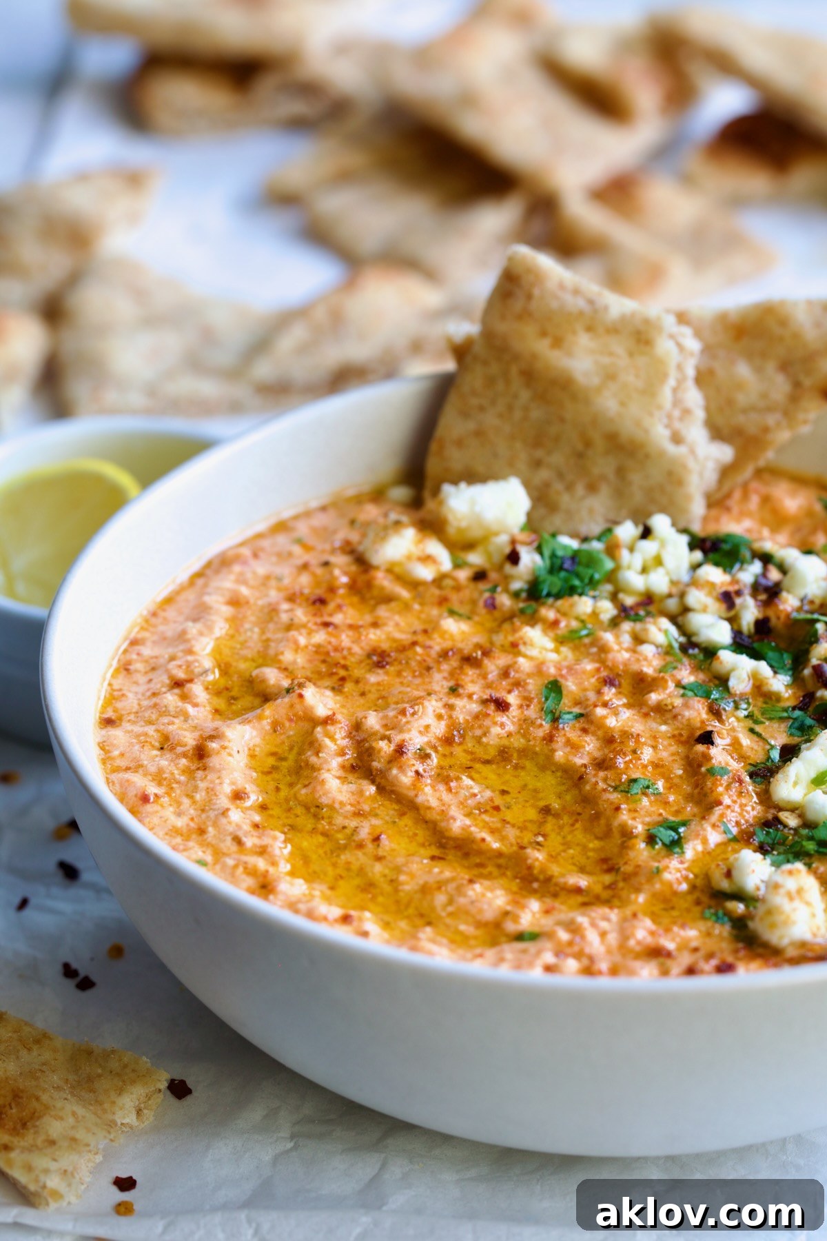 Spicy Feta Dip (Tirokafteri) in white bowl garnished with crumbled feta cheese and parsley surrounded by pita wedges.