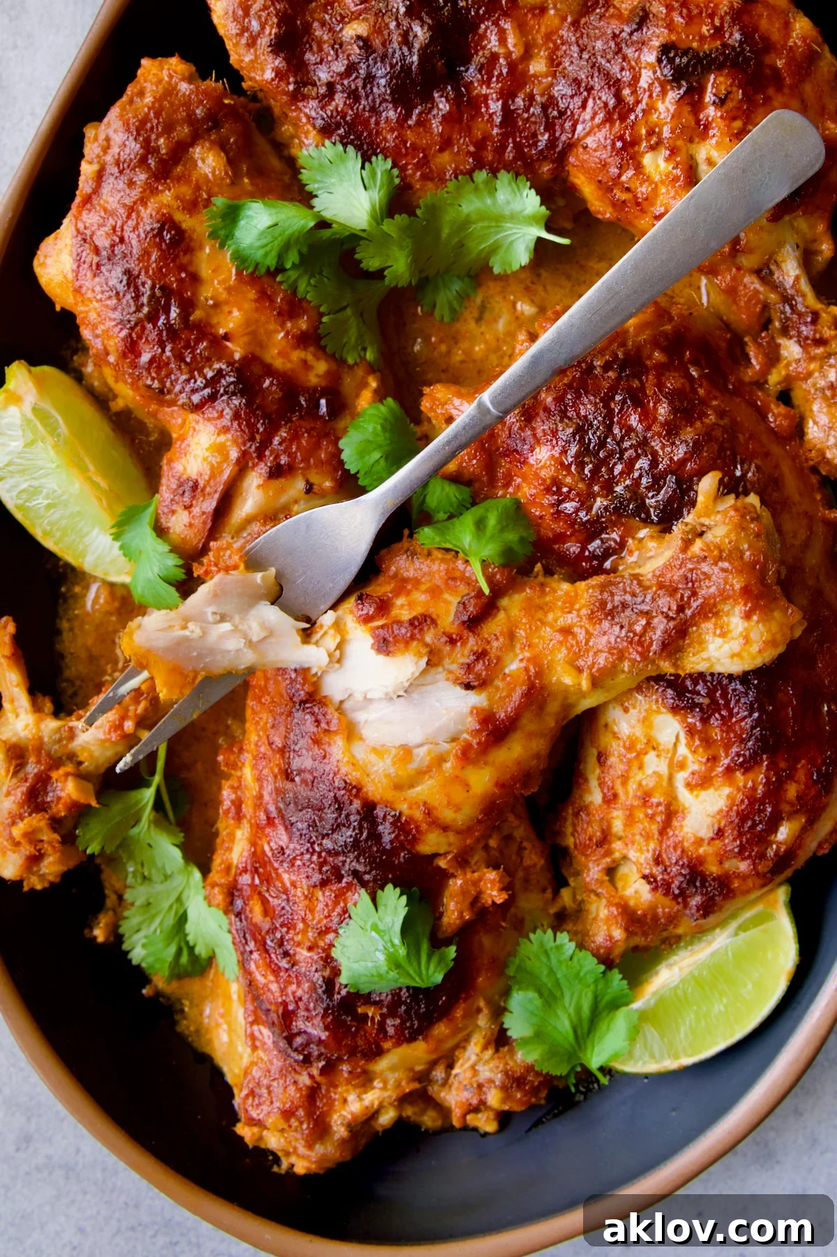 A final, enticing view of Thai Red Curry Braised Chicken Legs on a black platter, elegantly garnished with cilantro and lime, with a serving fork poised for the first bite.