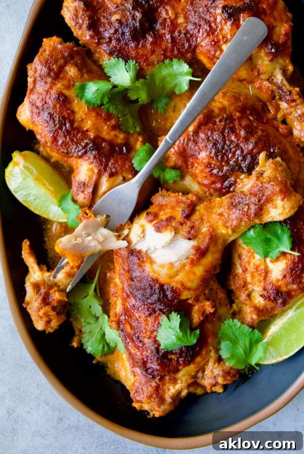 Thai Red Curry Chicken Legs on black platter garnished with cilantro and lime wedges with serving fork.