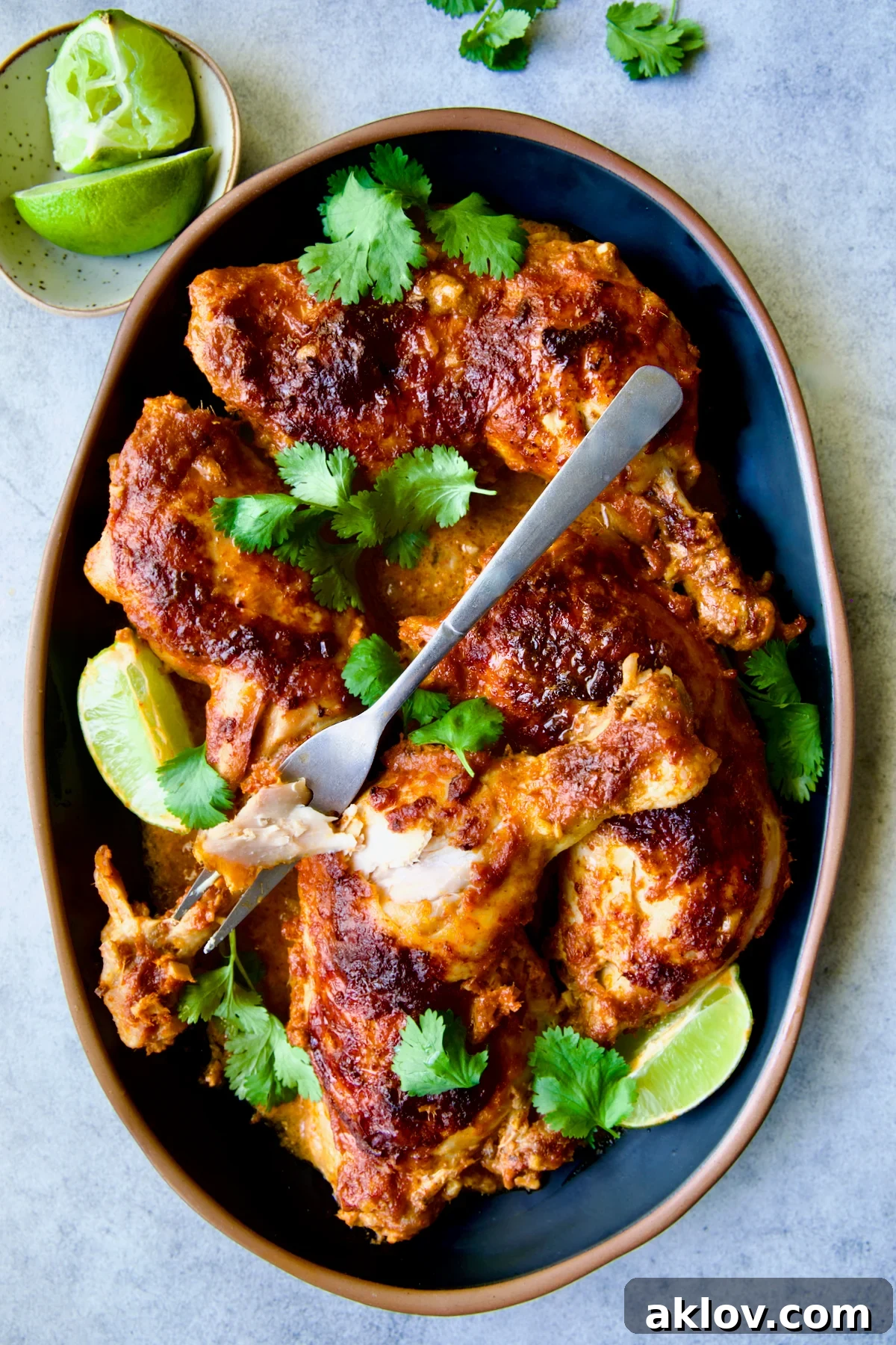 Spicy Thai Red Curry Chicken Drumsticks 3 Thai Red Curry Braised Chicken Legs on black platter garnished with cilantro and lime wedges with serving fork.