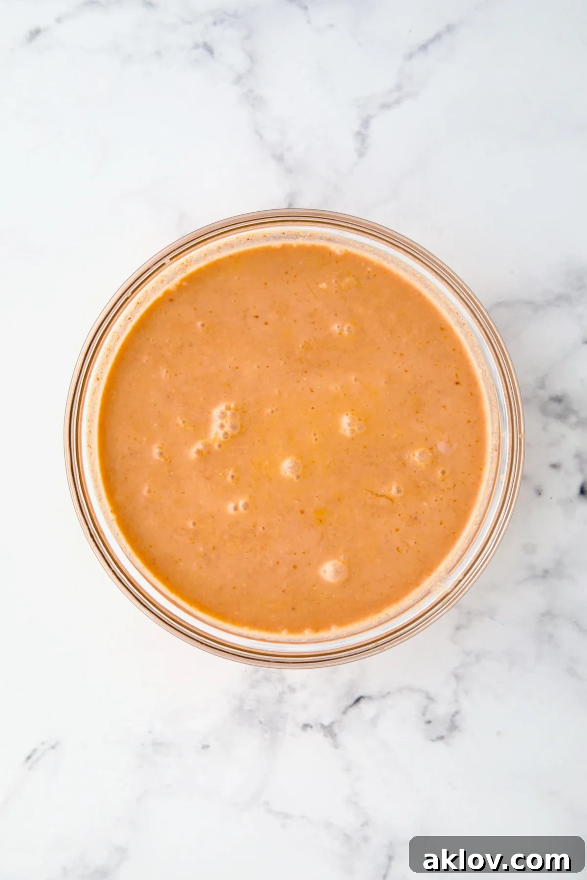 A glass bowl holds a vibrant mixture of coconut milk, red curry paste, minced garlic, fresh ginger, and savory fish sauce, perfectly combined and ready for the chicken.