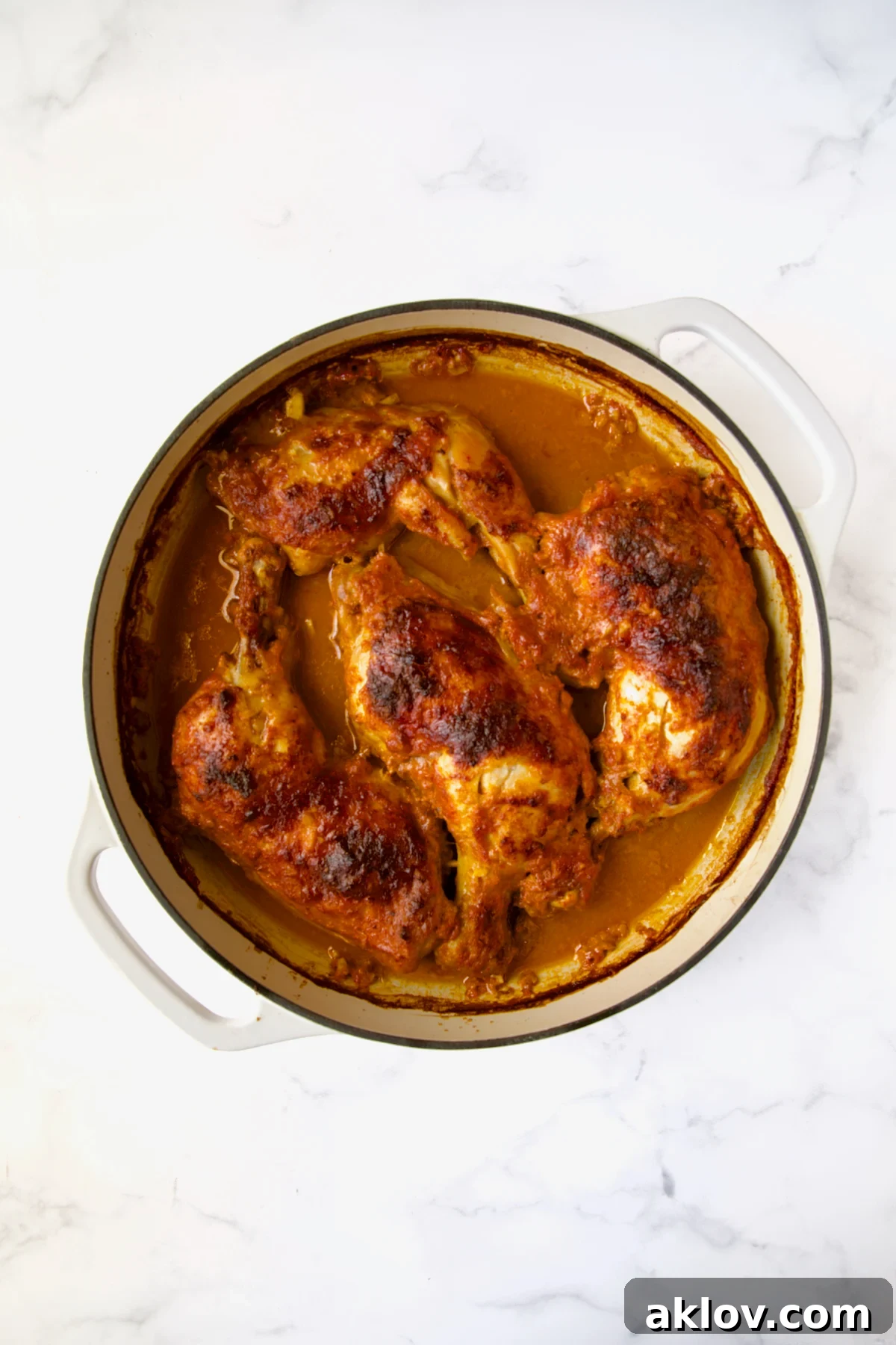 Perfectly braised chicken legs, golden and succulent, resting in a white enamel cast iron skillet straight from the oven, without any garnishes yet.