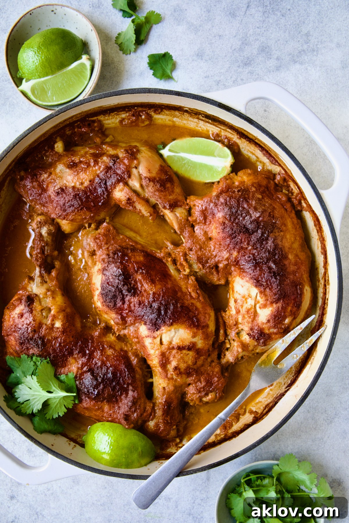 Spicy Thai Red Curry Chicken Drumsticks 8 Thai Red Curry Braised Chicken Legs in white enamel cast iron skillet garnished with cilantro and lime wedges with serving fork.