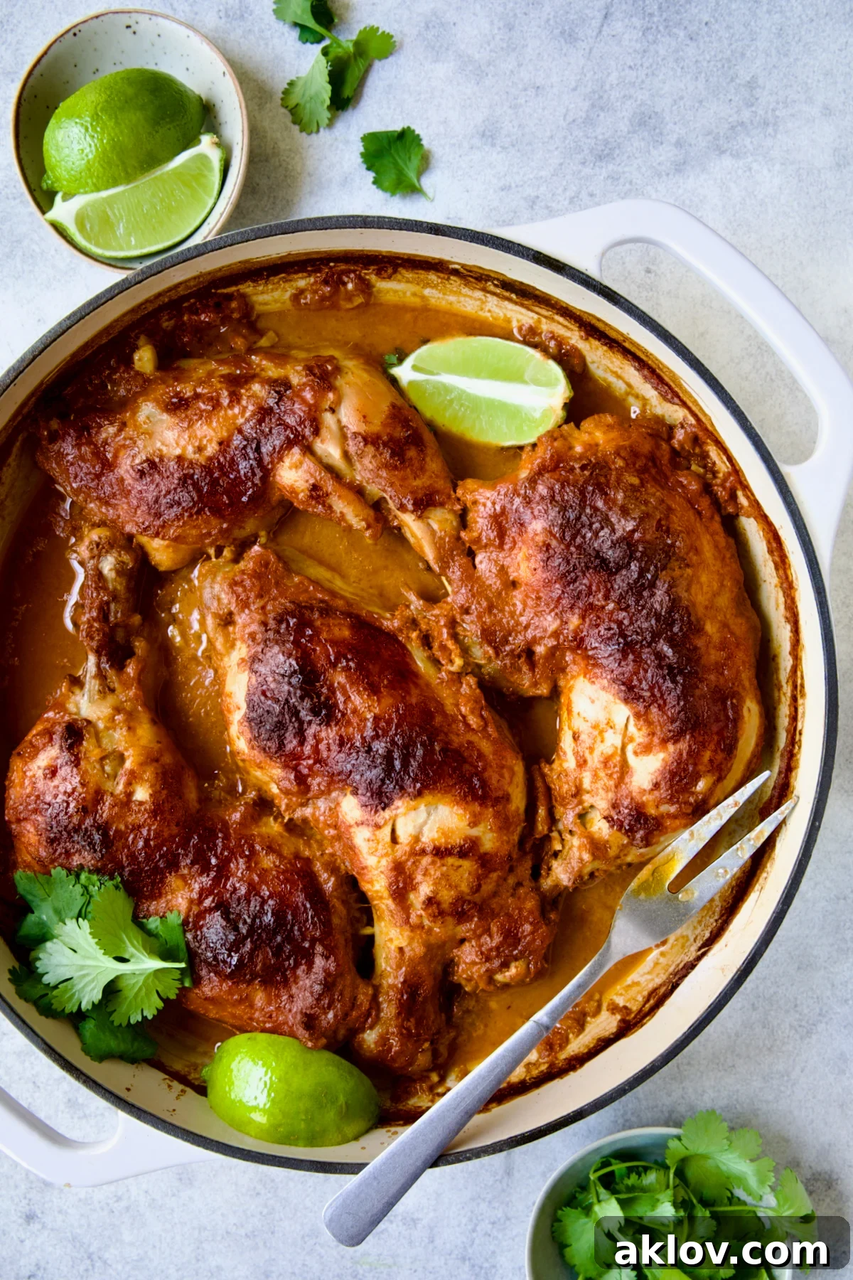 The finished Thai Red Curry Braised Chicken Legs, now elegantly presented in a white enamel cast iron skillet, beautifully garnished with fresh cilantro and lime wedges.