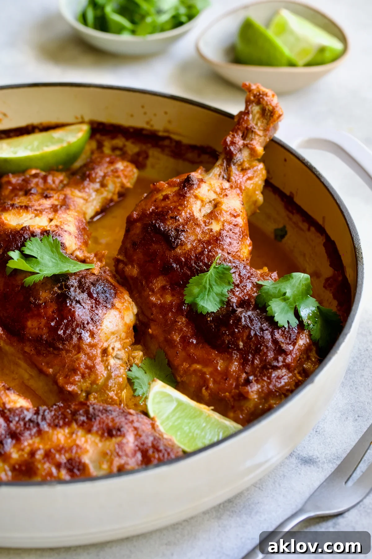 A final, mouth-watering shot of Thai Red Curry Braised Chicken Legs presented in a pristine white enamel cast iron skillet, garnished with fresh cilantro and lime, ready to be devoured.