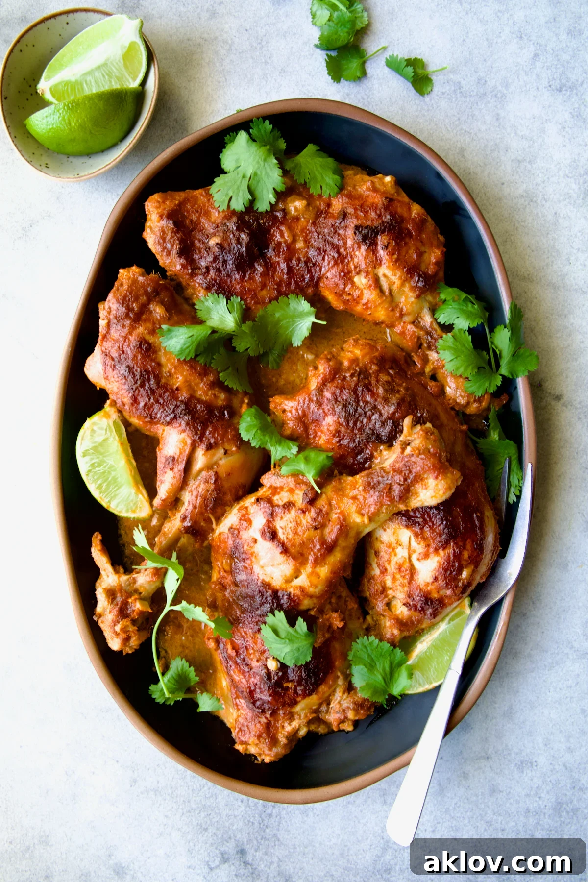 Spicy Thai Red Curry Chicken Drumsticks 10 Thai Red Curry Braised Chicken Legs on black platter garnished with cilantro and lime wedges with serving fork.