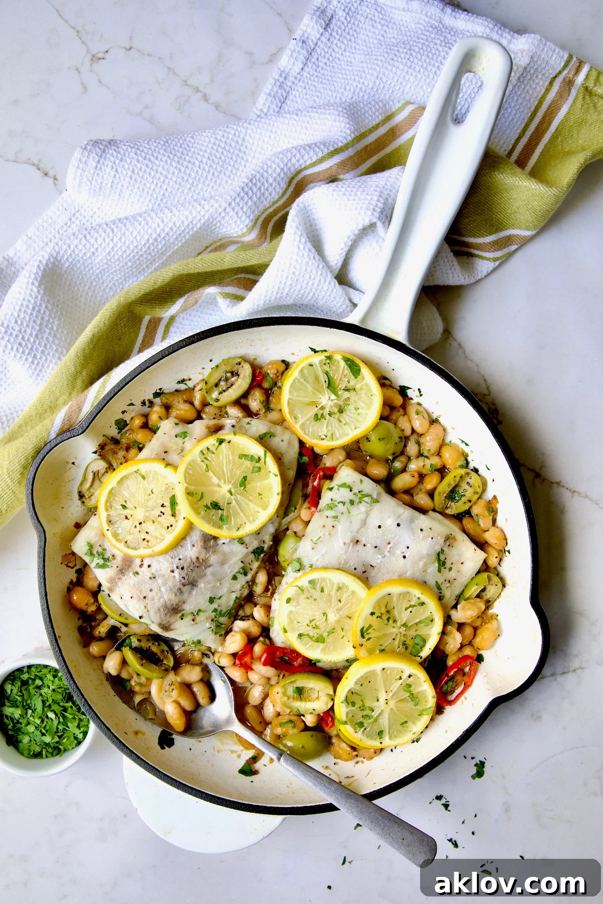 Mediterranean Fish and White Bean Skillet in white cast iron skillet topped with lemon slices sprinkled with fresh parsley.