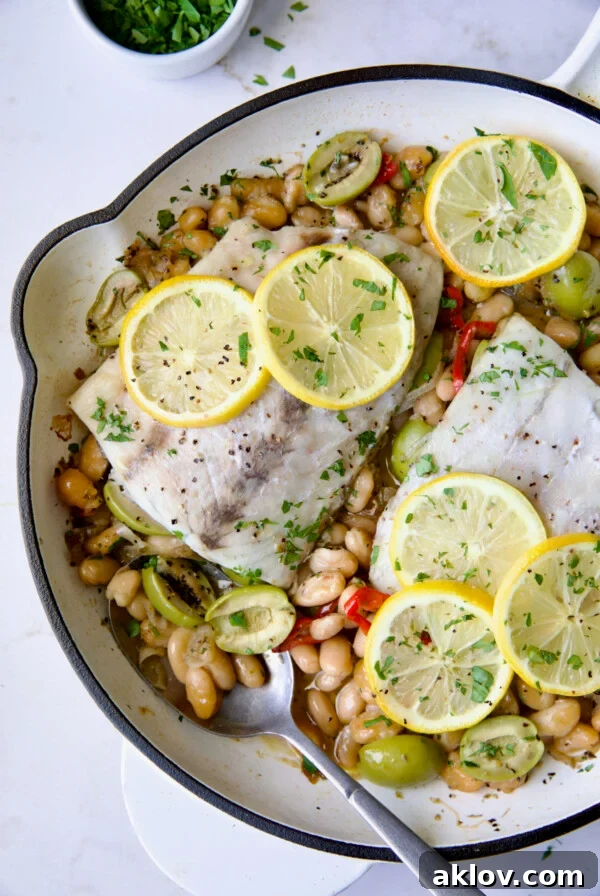 Mediterranean Fish and White Bean Skillet in white cast iron skillet topped with lemon slices.