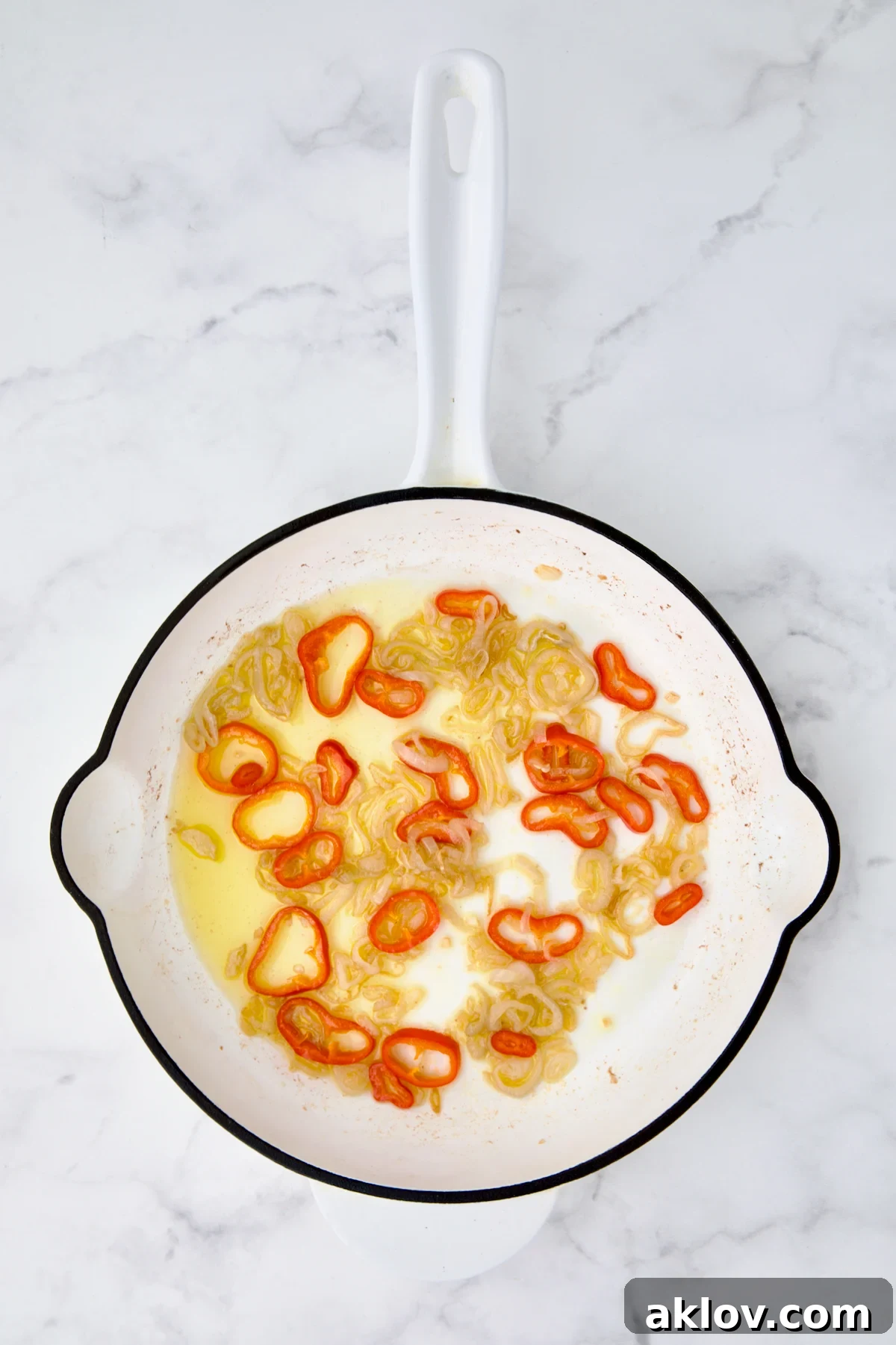 Sauteed shallot rings and Fresno chile in white cast iron skillet in olive oil.