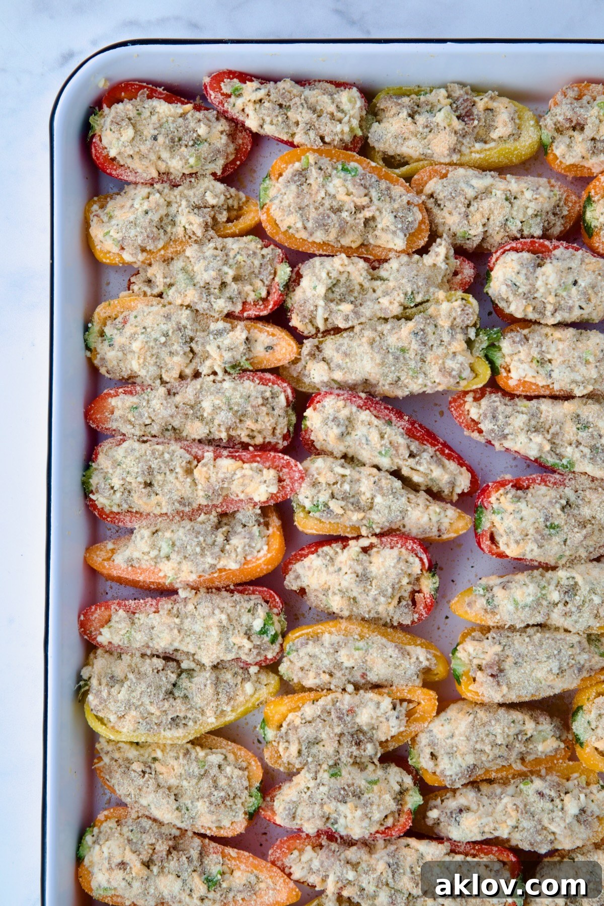 Stuffed mini peppers on a white enamel rimmed baking sheet, lightly sprinkled with Italian breadcrumbs, ready for the oven.