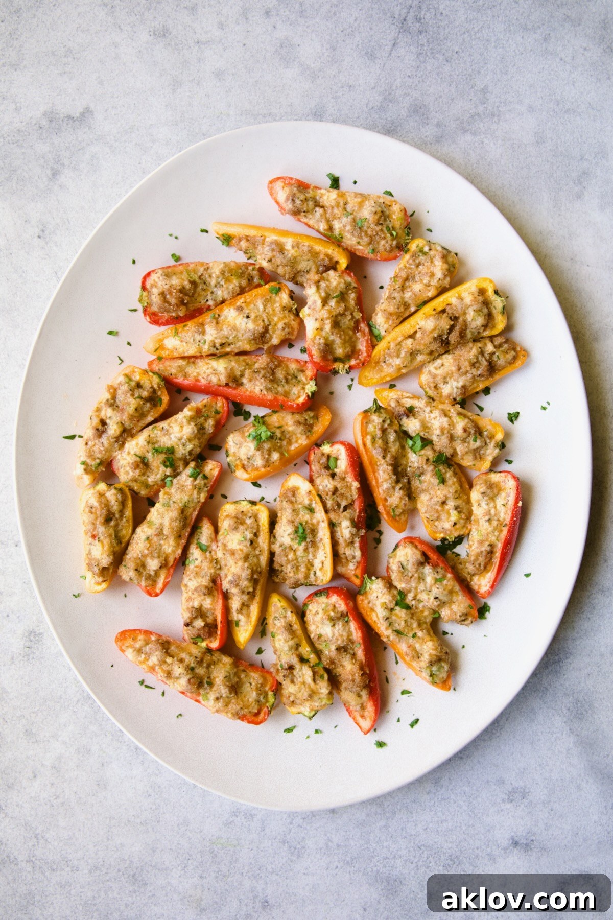 Stuffed Mini Peppers elegantly arranged on a white oval platter and garnished with fresh chopped parsley, ready for guests.