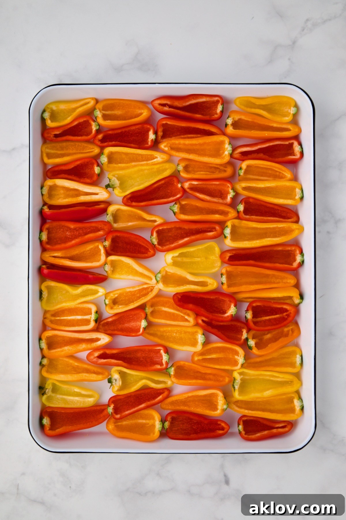 Halved mini sweet peppers arranged neatly on a white enamel rimmed baking sheet, ready for filling.