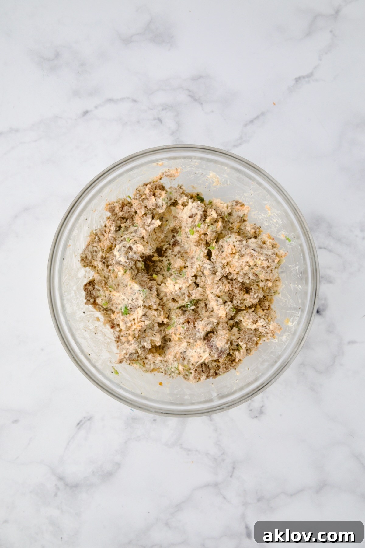 The sausage, cream cheese, and Mexican blend cheese mixture after being thoroughly combined in a glass bowl.