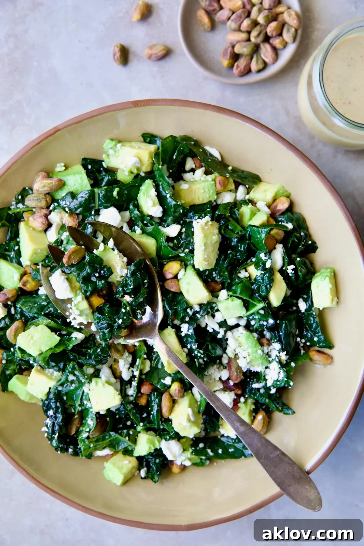 Tuscan Kale Salad with Lemon Tahini Dressing in beige bowl with serving spoon.