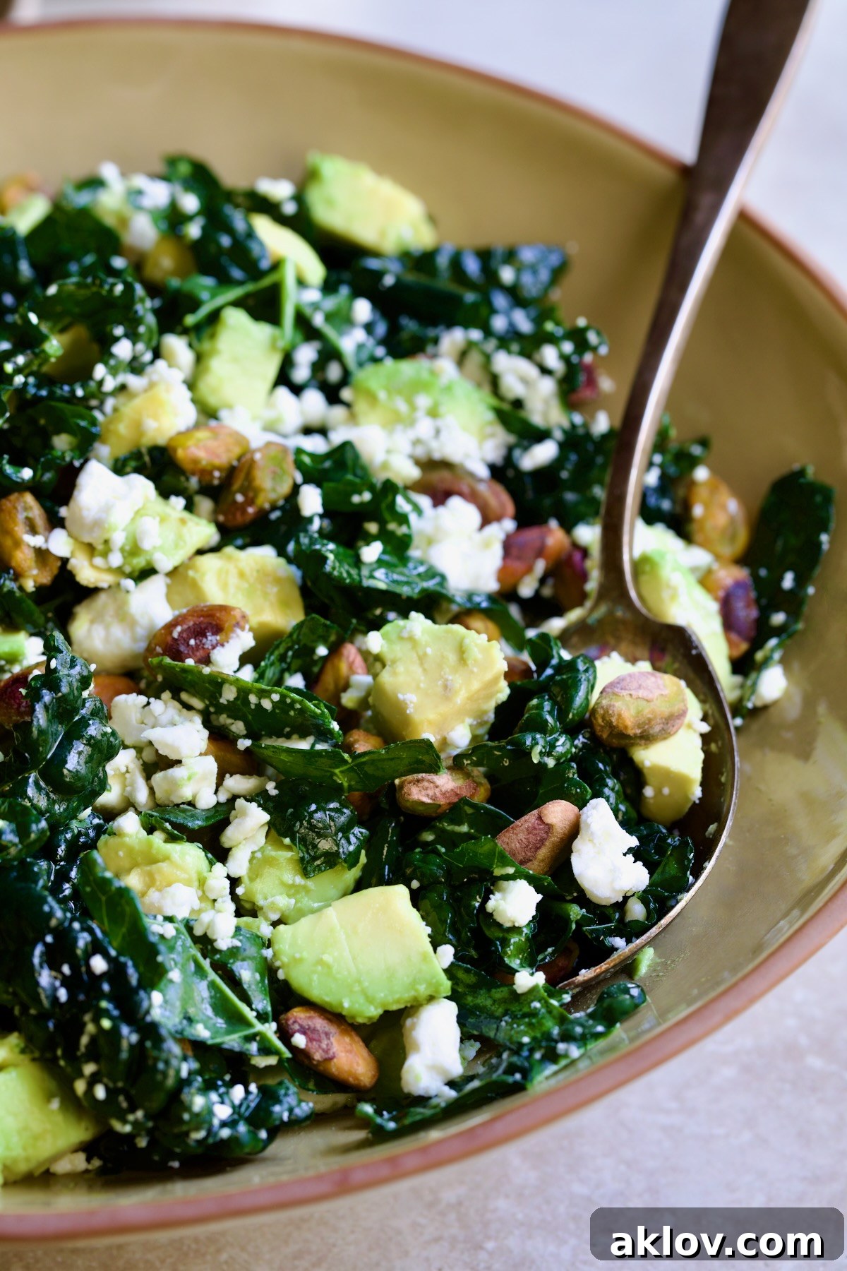 Tuscan Kale Salad with Lemon Tahini Dressing in beige bowl with serving spoon scooping some up.