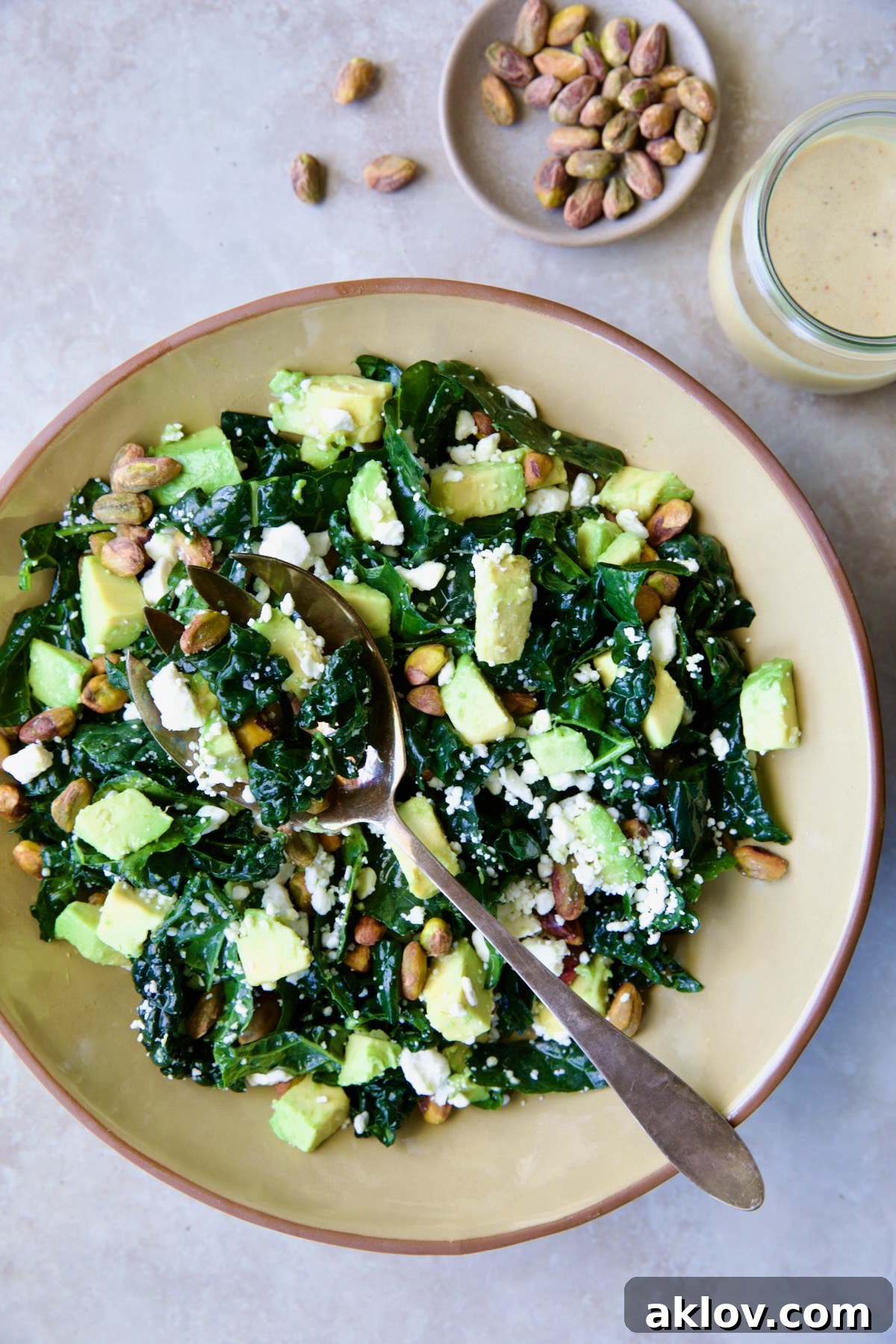 Tuscan Kale Salad with Lemon Tahini Dressing in beige bowl with serving spoon.