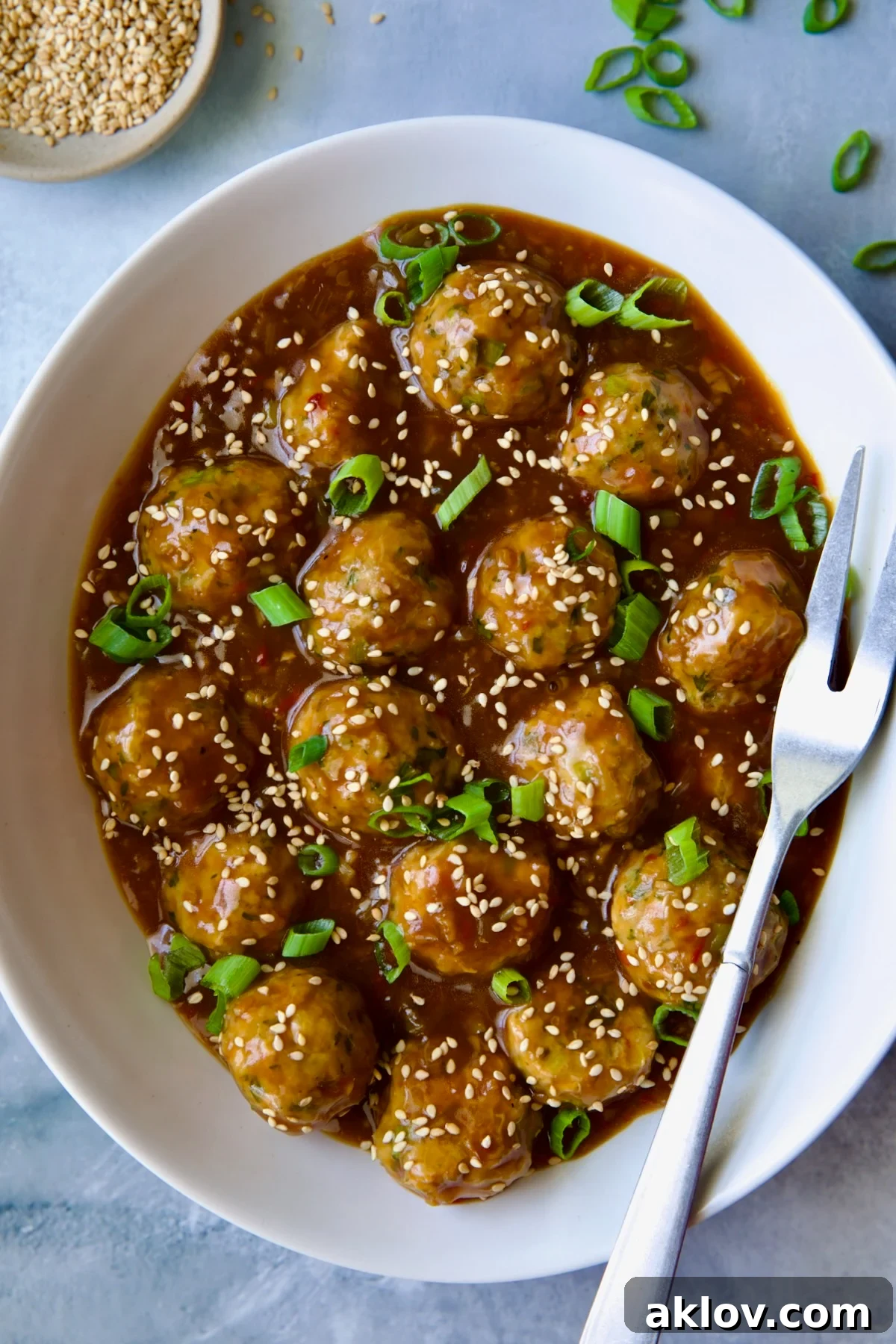 Flavorful Asian Turkey Meatballs served in a white oval bowl, garnished with toasted sesame seeds and fresh scallions, ready for serving.