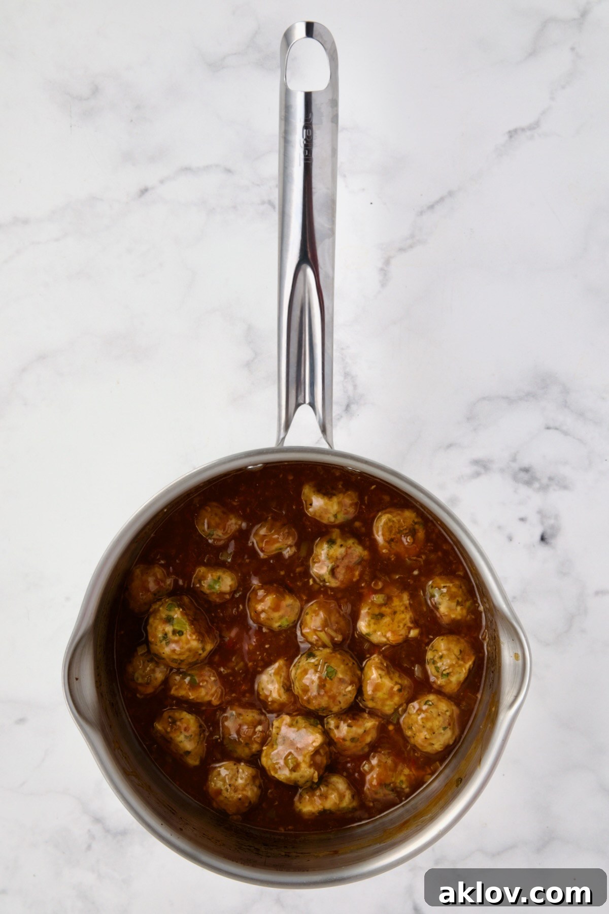Baked turkey meatballs being tossed with the glistening Orange Sesame Sauce in a stainless steel saucepan.