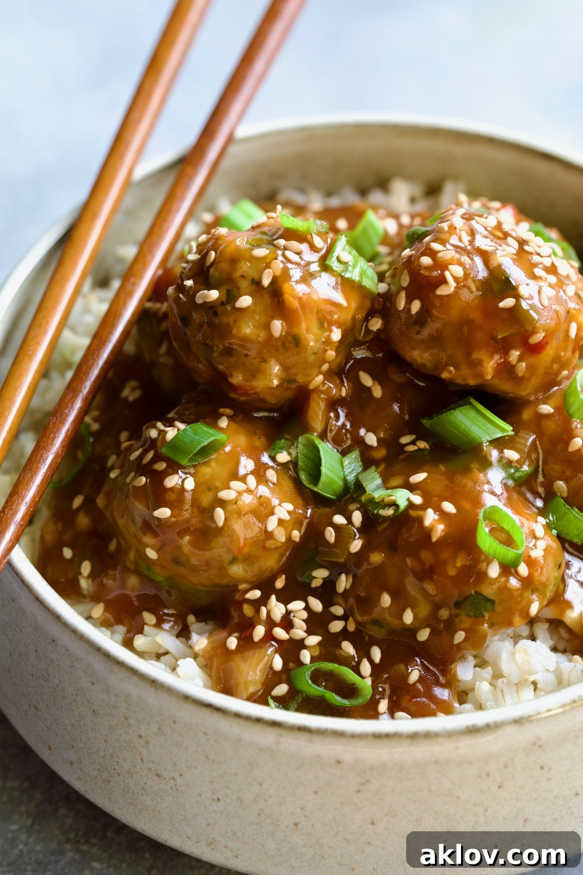 Asian Turkey Meatballs served over a bed of brown rice in a bowl, garnished with chopsticks, sesame seeds, and scallions.