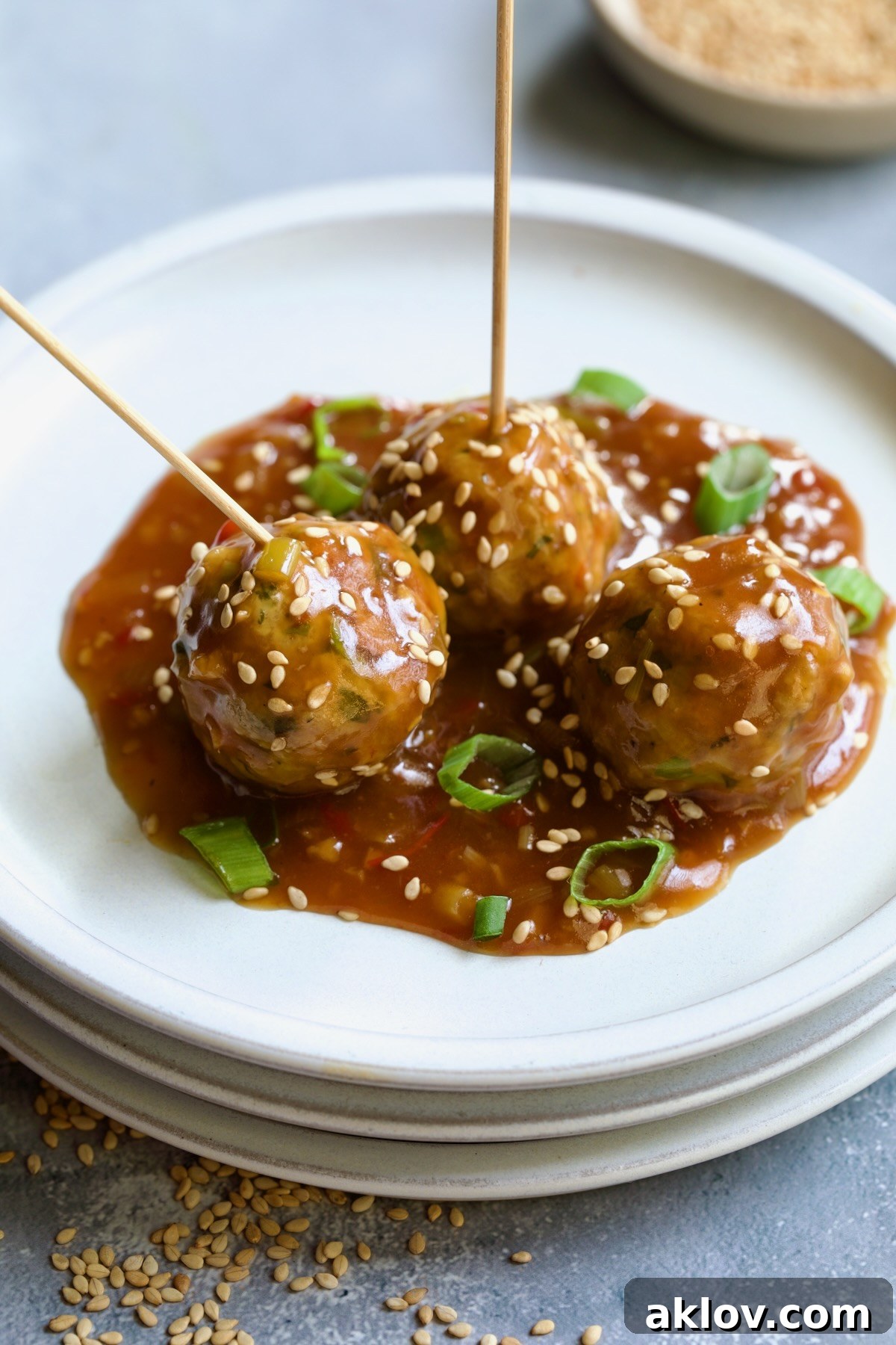 Three Asian Turkey Meatballs on small appetizer plates, each with a serving pick, garnished with sesame seeds and scallions.