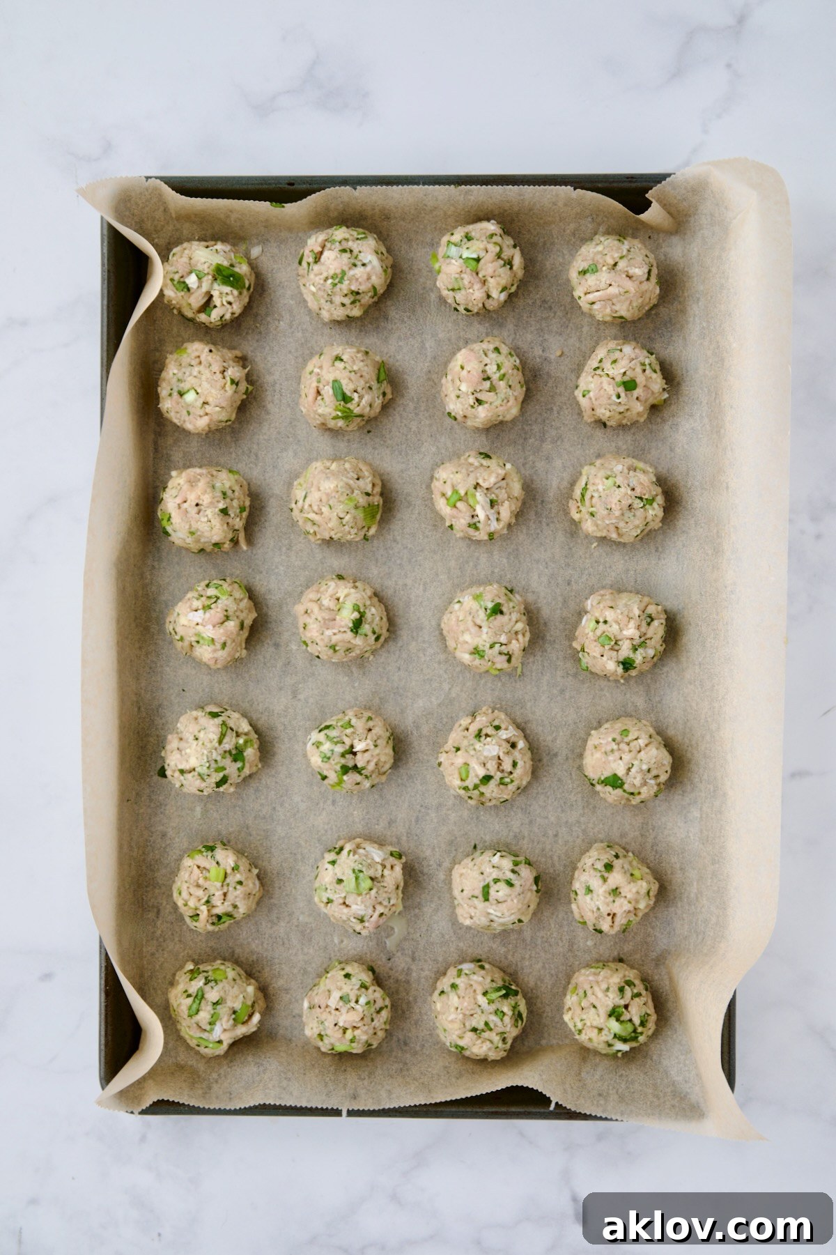 Raw turkey meatballs neatly arranged on a parchment paper-lined baking sheet, ready to be baked.
