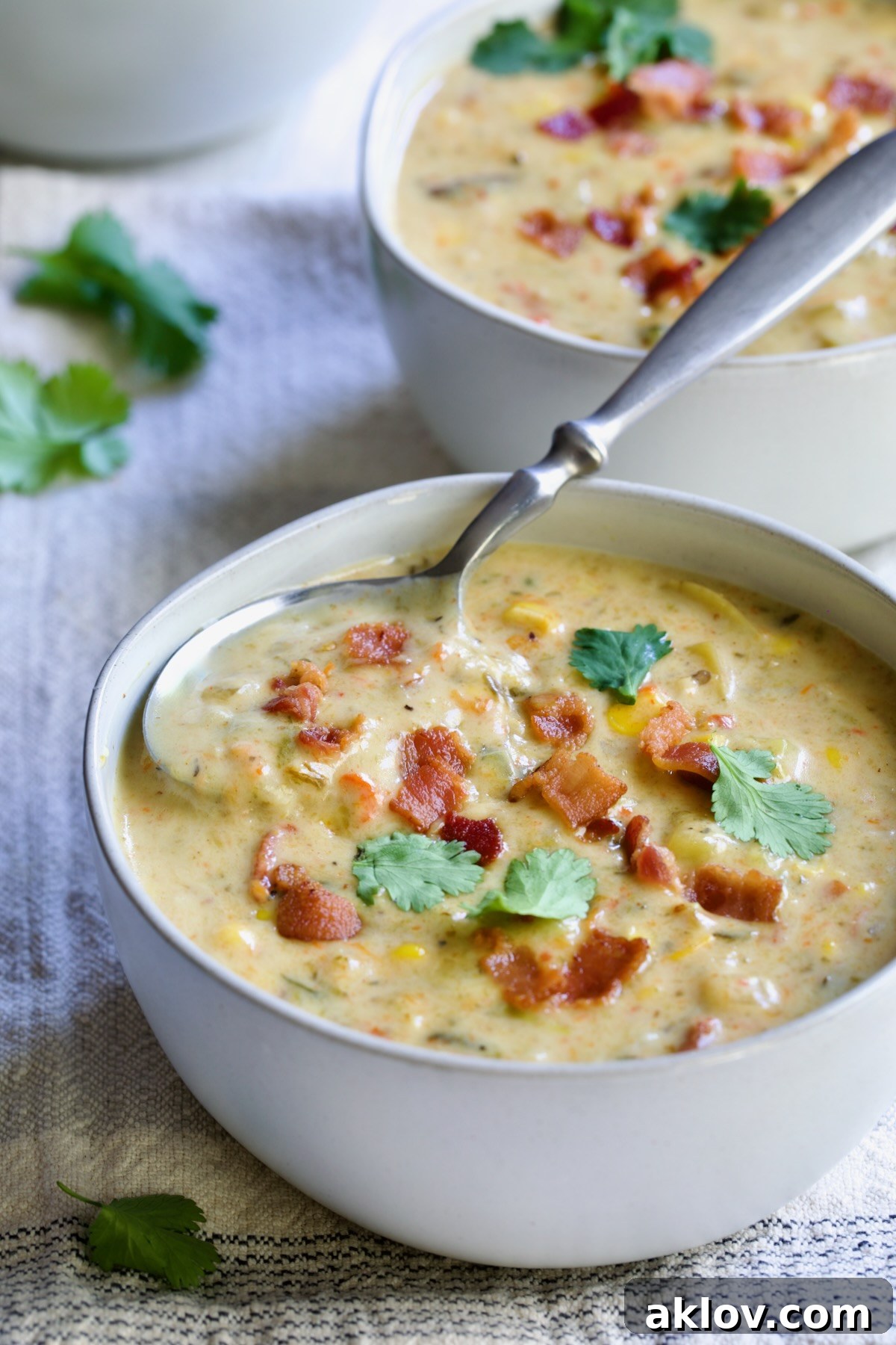 A comforting bowl of Roasted Poblano Corn Chowder, garnished with fresh cilantro sprigs and a soup spoon ready to dive in.